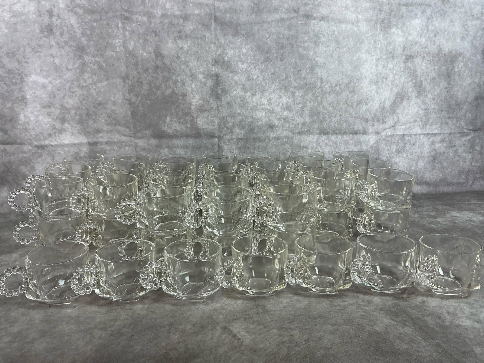Hazel Atlas Punch Cups: Fifty-five 1950's clear pressed glass cups. "Sip and Smoke" square based cup with beaded handle. In good condition. Cups measure 2.75 inches in diameter at rim x 2.5 inches tall.