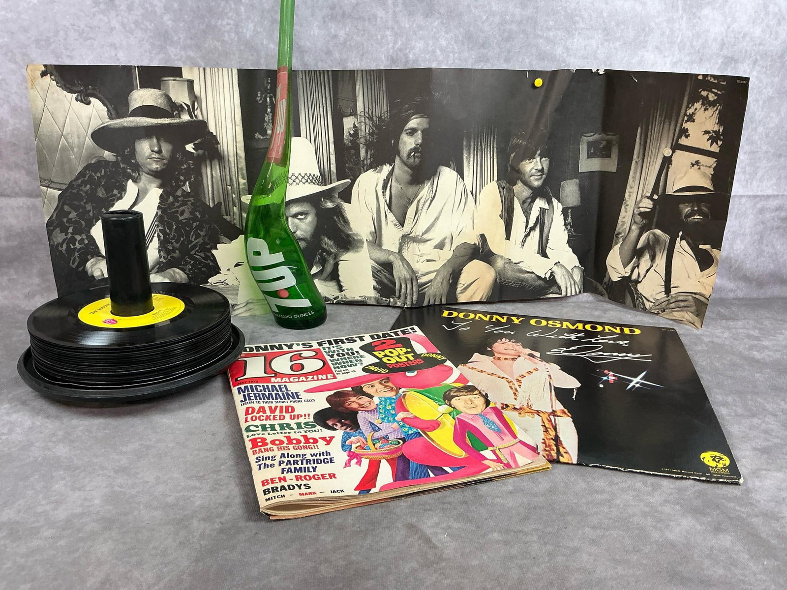 1970's Records, Poster, Teen Magazine, & Bottle: Four items and eighteen 45 rpm records from the 1970's. The Eagles 1974 poster from Hotel California Album, and "16 Magazine " 1972 featuring Donny Osmond, David Cassidy, and more. Includes stretched