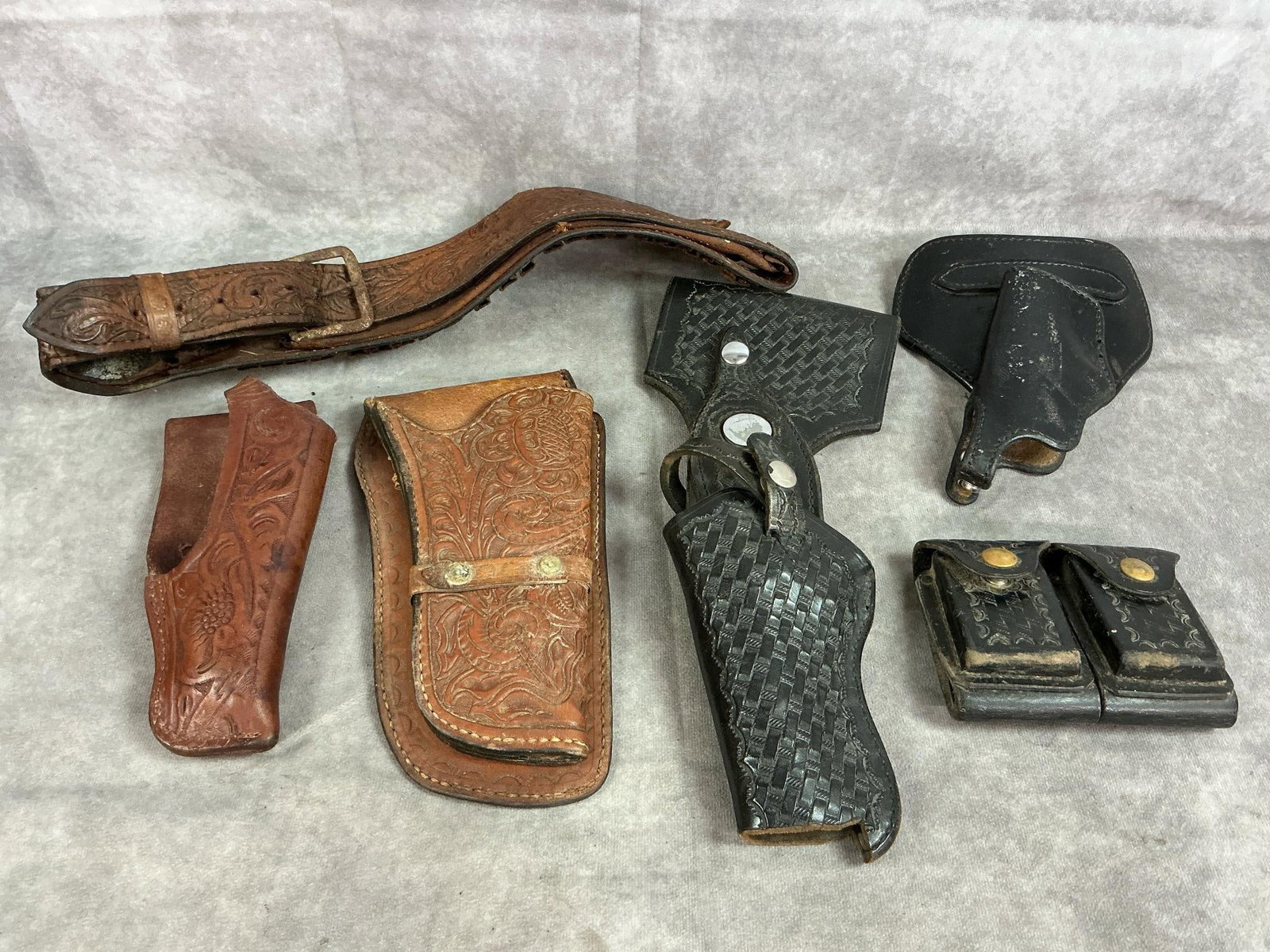 Leather Gun Holsters: Six vintage leather holsters, ammo pouch, and belt. Black patrolman's basket weave holster and pouch by Bucheimer, ammo belt and brown holster, and more. Some rust and wear present. Black belt loop