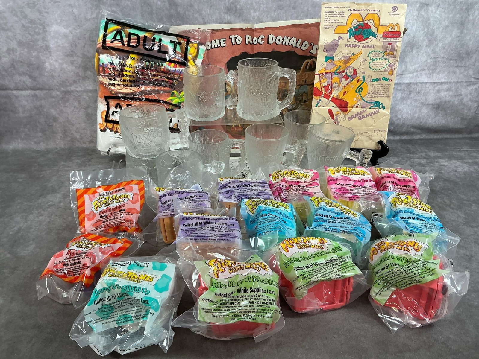 Meet the Flintstones! Collectibles: Twenty-five 1993-1994 McDonald's Happy Meal toys and glassware. Fifteen toys, nine TreeMendous mugs, and an adult XL Flintstones t-shirt. Toys and t-shirt in original packaging. Mug average size 3