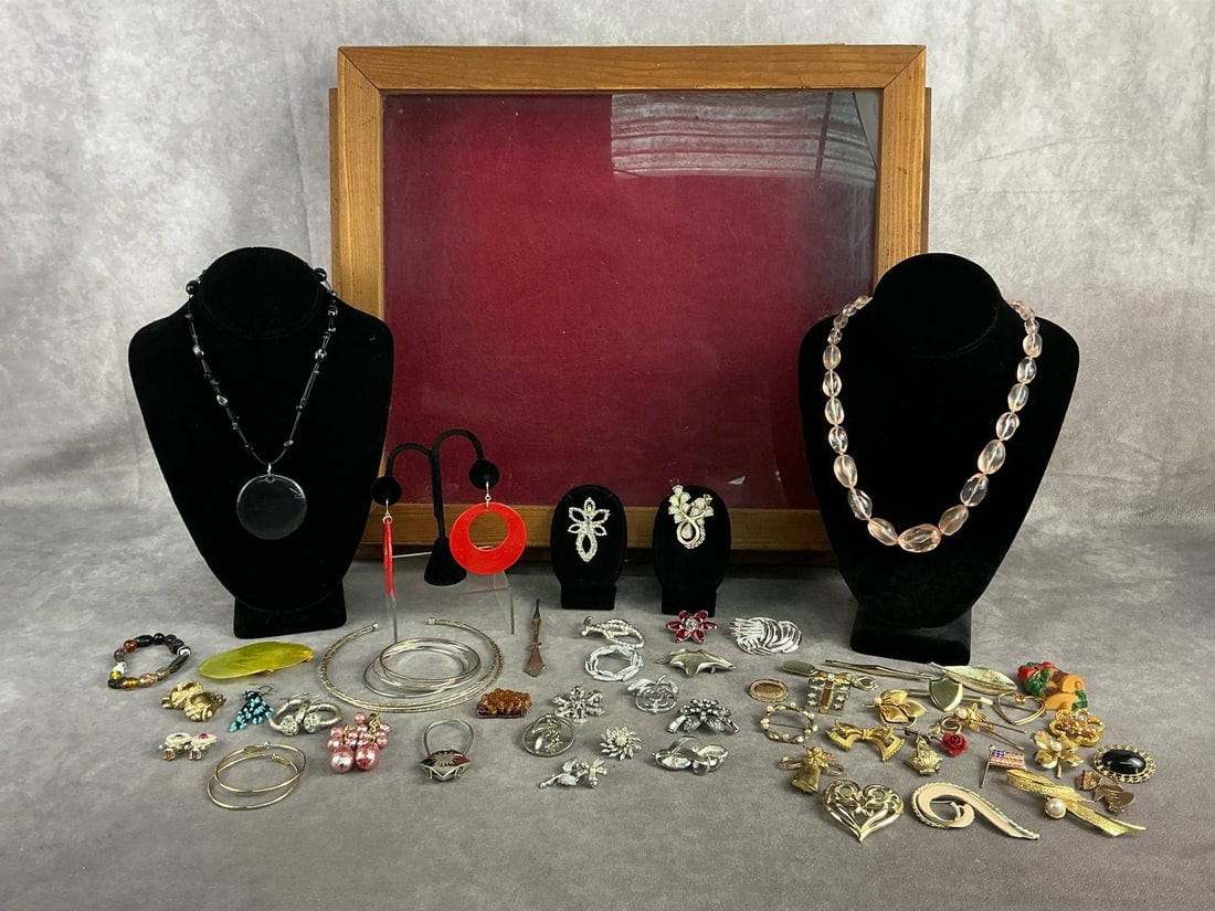 Costume Jewlelry: Large display case with costume jewelry including three necklaces, eight earrings, two bracelets, and thirty six brooches. All in good condition. Display measures 19.5 inches wide x 15.5 inches tall.