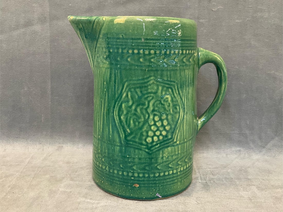 McCoy Stoneware Pitcher: Circa 1920's Nelson McCoy Stoneware Pottery Pitcher with grape and shield relief decoration. Good condition. Measures 8 inches wide x 5.5 x 8.75 inches tall.
