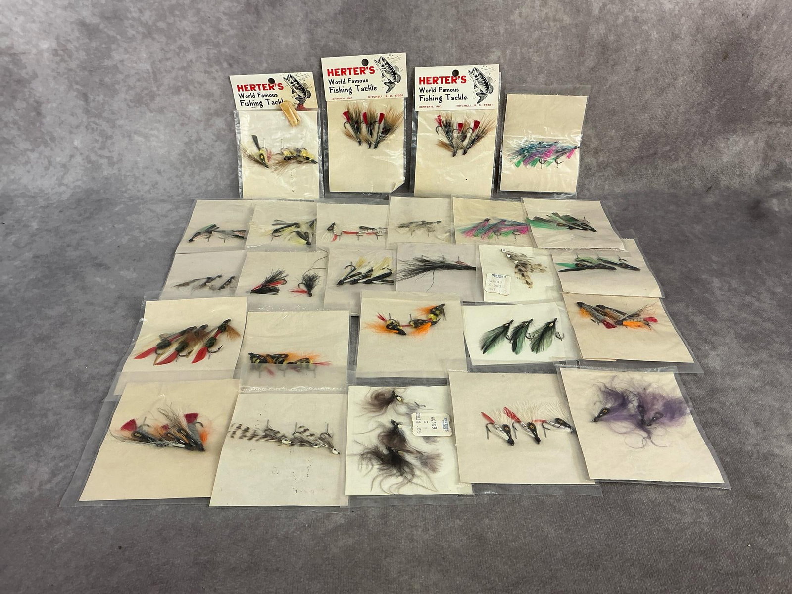 : Twenty six 1960s/1970s Herter's fly fishing lures in original packaging. Only three have their original hanging card, good condition. Measures 3.25 inches wide x 4.5 inches tall.