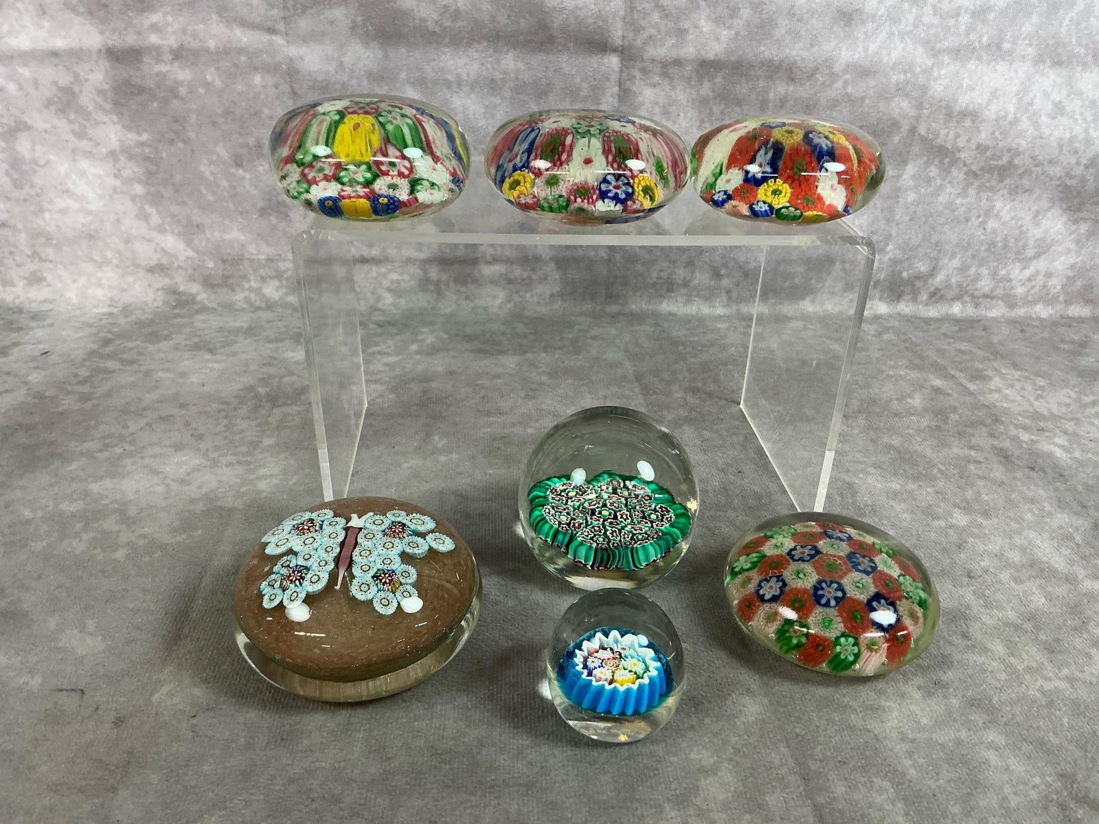 Millifiori Glass Paperweights: Seven vintage paperweights. Murano butterfly and floral designs in assorted colors in millifiori glass. In good condition. Butterfly measures 3 inches across x 1.5 inches tall.
