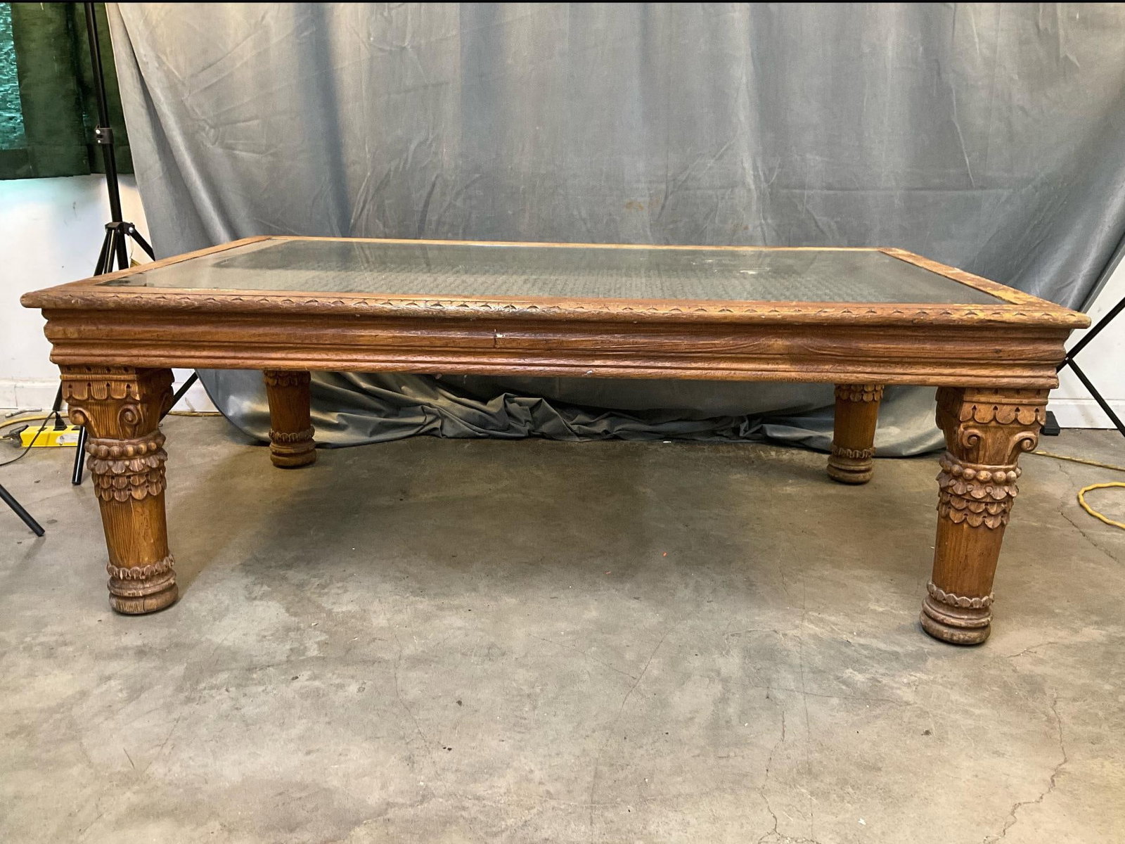 Glass Coffee Table: Circa 1970's - 1980's carved coffee table with iron grate inset and glass top. Wear and loss to finish, otherwise good condition. Measures 60 inches wide x 37 x 21.5 inches tall.