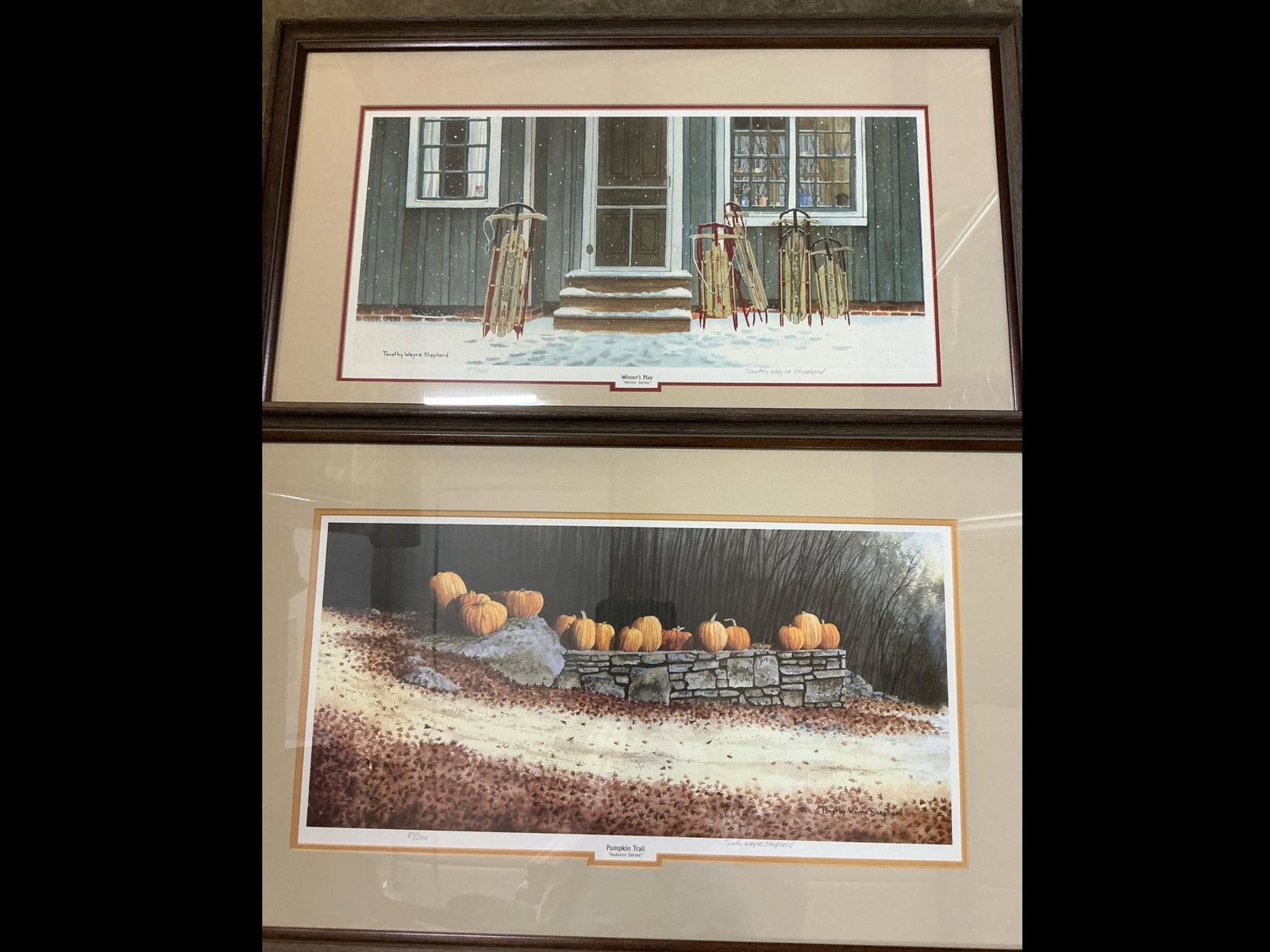 Seasonal Prints: Two matted and framed art prints by Timothy Wayne Shepherd. "Winter's Play" and "Pumpkin Trail" watercolor prints numbered 87/300. Both in good condition. Measures 31 inches wide x 1 x 20 inches tall.