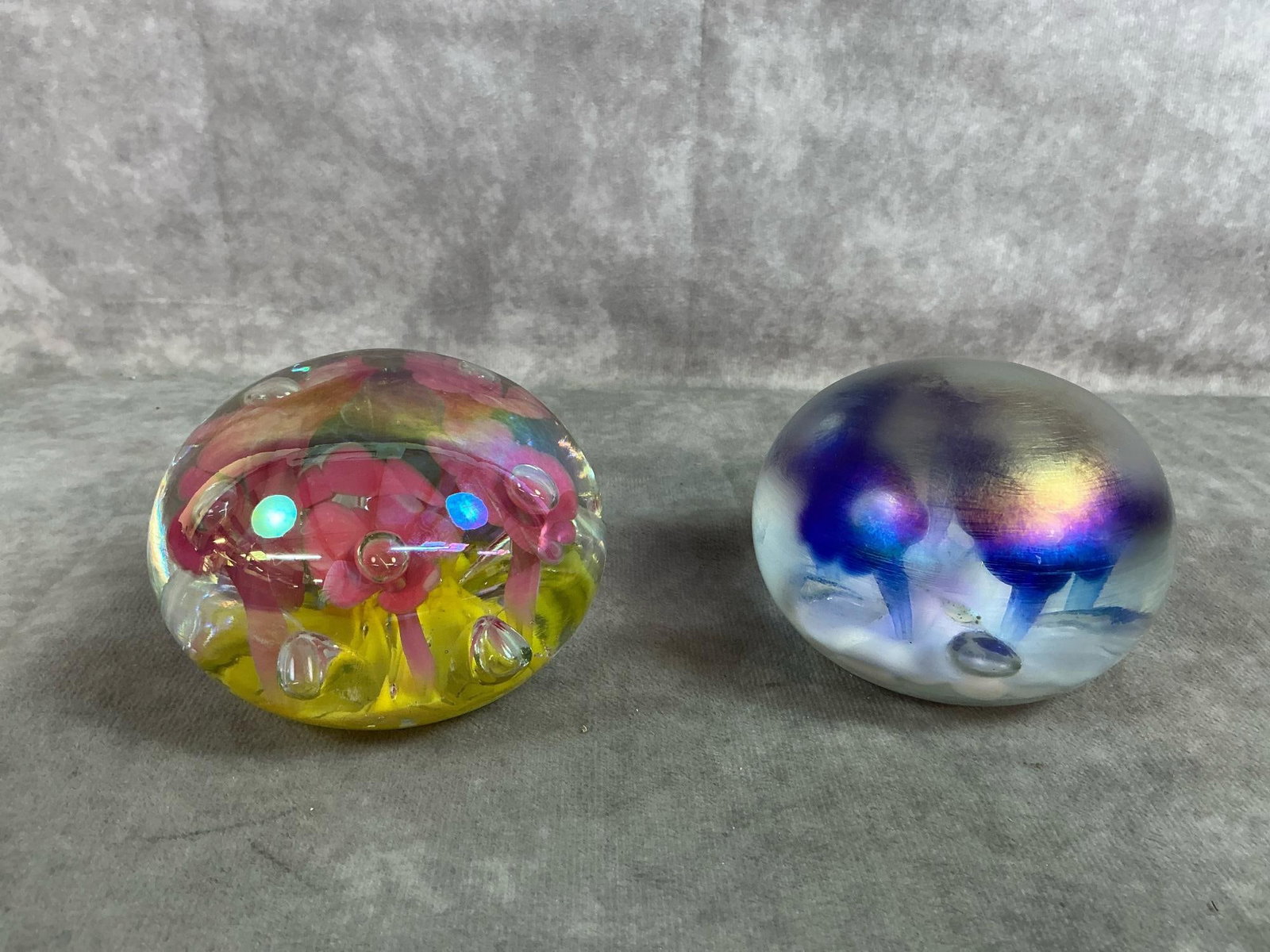 St Clair Paperweights: Two Joe St Clair glass paperweights. Frosty blue blooms art glass and pink blooms with yellow in clear glass. In good condition. Measure 3.5 inches wider 3 inches tall.