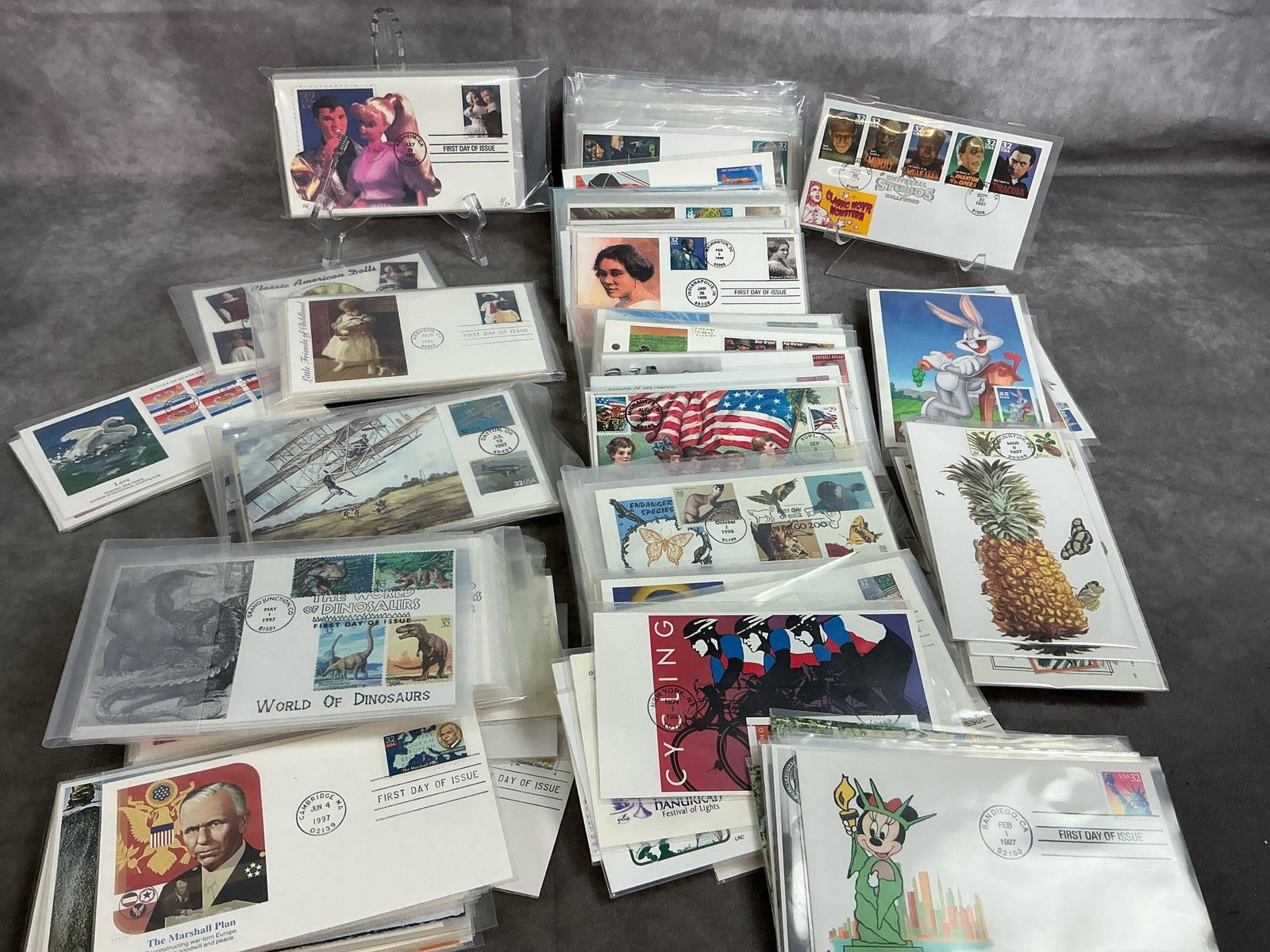 Fun and Collectible First Day Issues: Several hundred First Day Covers from 1990's. Includes entertainers, planes, movie monsters, tigers, dolls and dinosaurs. Protected in clear sleeves. Measures 6.5 inches wide x 4 inches tall.