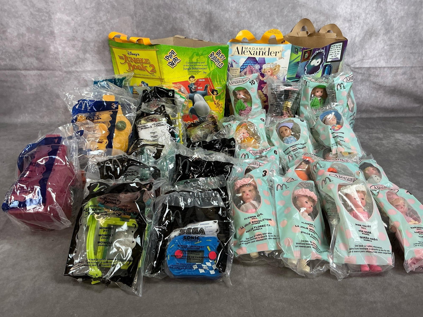 Collectible Happy Meal Toys: Thirty-eight 2003 McDonald's Happy Meal toys. Includes Madame Alexander dolls, Sega Sonic games, Hotwheels Highway 35, and Jungke Book 2 toys. In original packaging. Average package measures 4 inches 