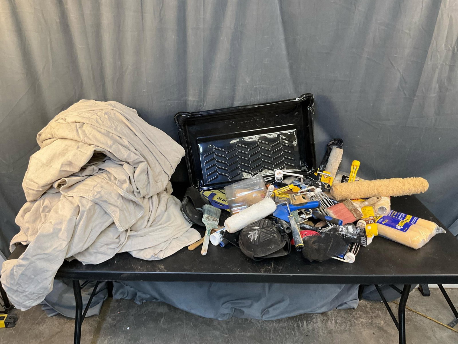 Painting Supplies: Assortment of painting contractor tools including; 3 canvas drop cloths, paint brushes, knee pads, Purdue unused tray, rollers and caulk gun with caulk. Mostly used condition with some unused paint