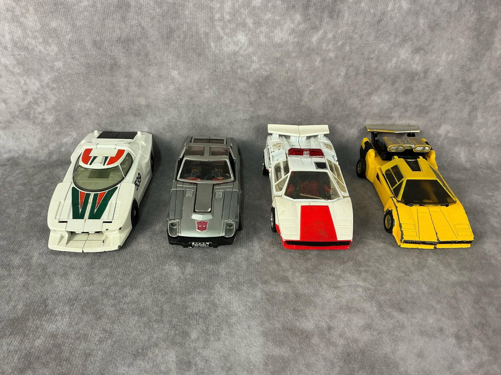 1980s Transformers: Four 1982 generation one Transformers made by Takara in Japan. Includes Wheeljack, Red Alert, Blue Streak, and Sunstreaker. All have wear and some paint loss. Largest measures 4.5 inches long x 2 x
