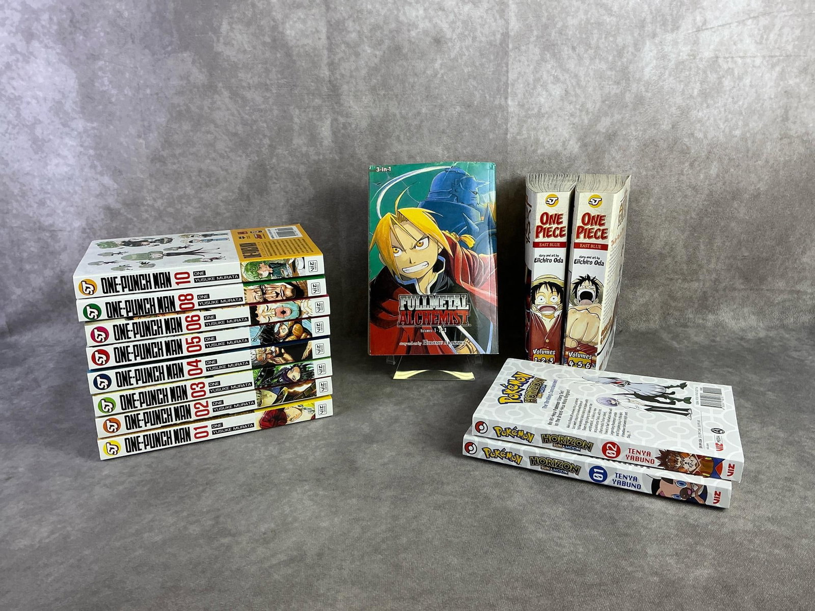 Manga: Thirteen manga including One Piece, Full Metal Alchemist, Pokemon, and One Punch Man. All in good condition and dating from 1997 through 2012. Largest measures 5 inches wide x 7.5 inches tall.