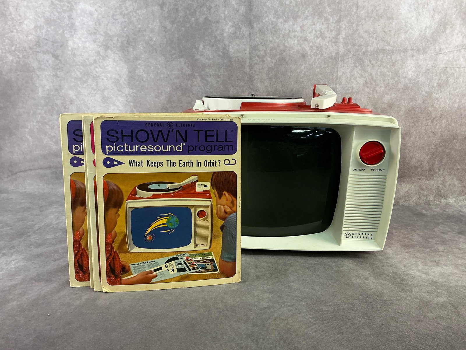 GE Show & Tell: 1964 GE Show N Tell four speed record player with slide a film viewer and includes nine show n tell vinyls with slide view film. In fair to good condition, does power on but has damage to record