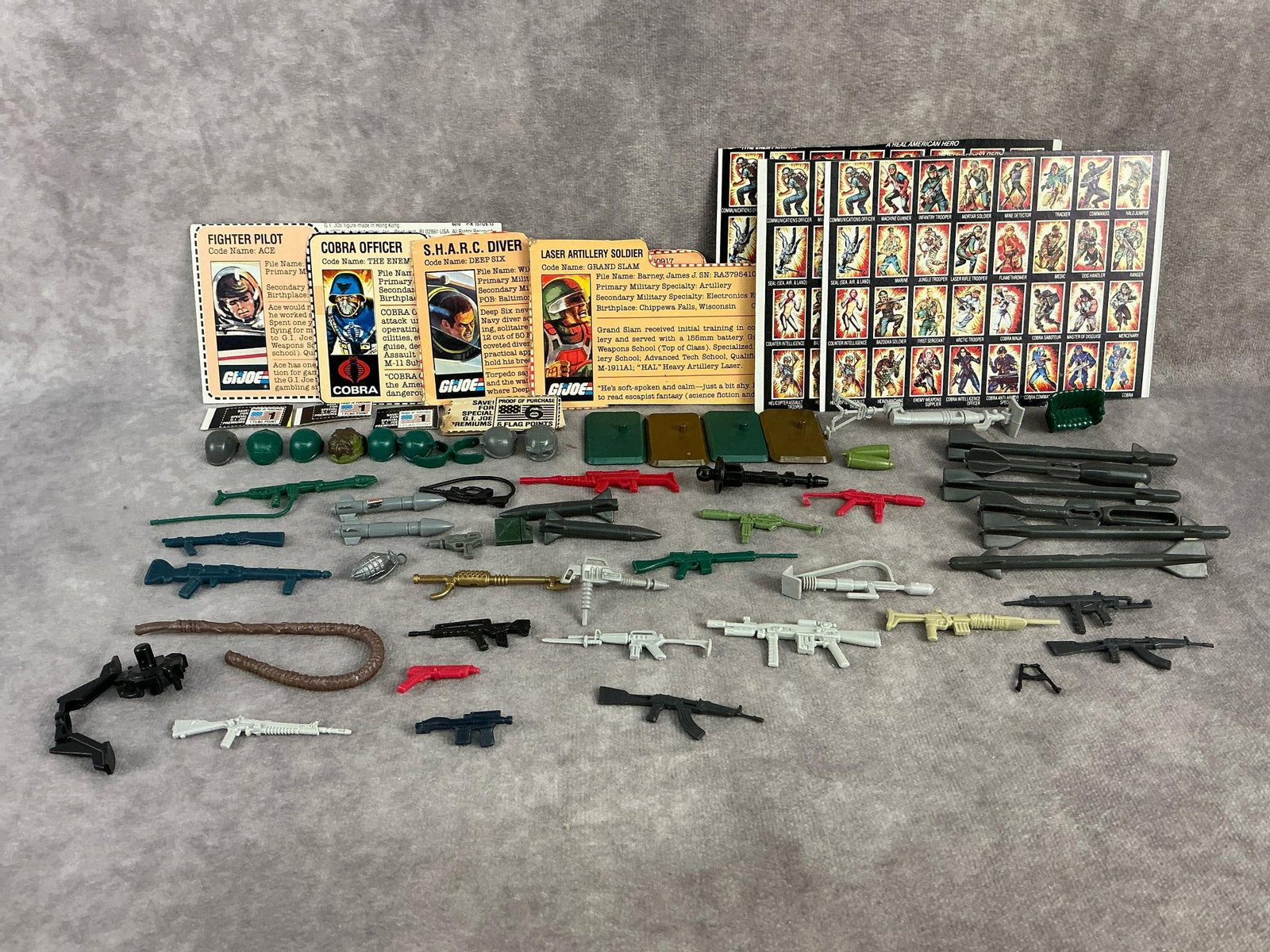 Action Figure Accessories: Large lot of vintage action figure weapons, accessories, and parts. Includes four GI Joe file cards, three GI Joe cardboard backs, helmets, weapons, stands, and other parts and accessories. Fair to