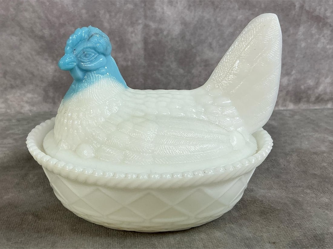 Blue Head Hen on Nest: Vintage Westmoreland milk glass hen on nest dish. Light blue head on textured basket base. Small darkened rough spot on bottom edge, otherwise In good condition. Measures 5.5 inches long x 4.25 x 4.5 
