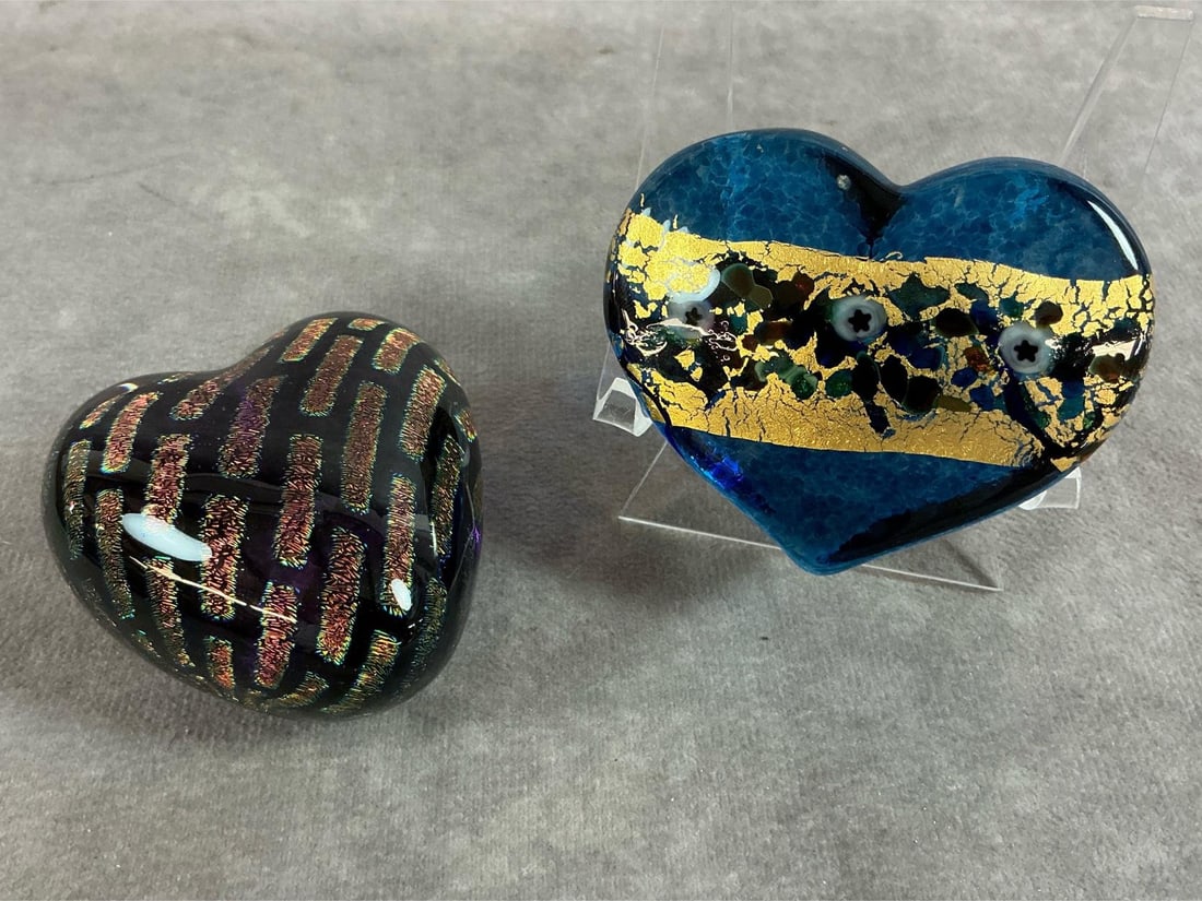 Heart Shaped Art Glass by Held: Two vintage heart paperweights. Blue with floral and gold leaf, and black with iridescent strips. Signed by Robert Held. In good condition. Blue one measures 3 inches wide x 2.25 inches tall.