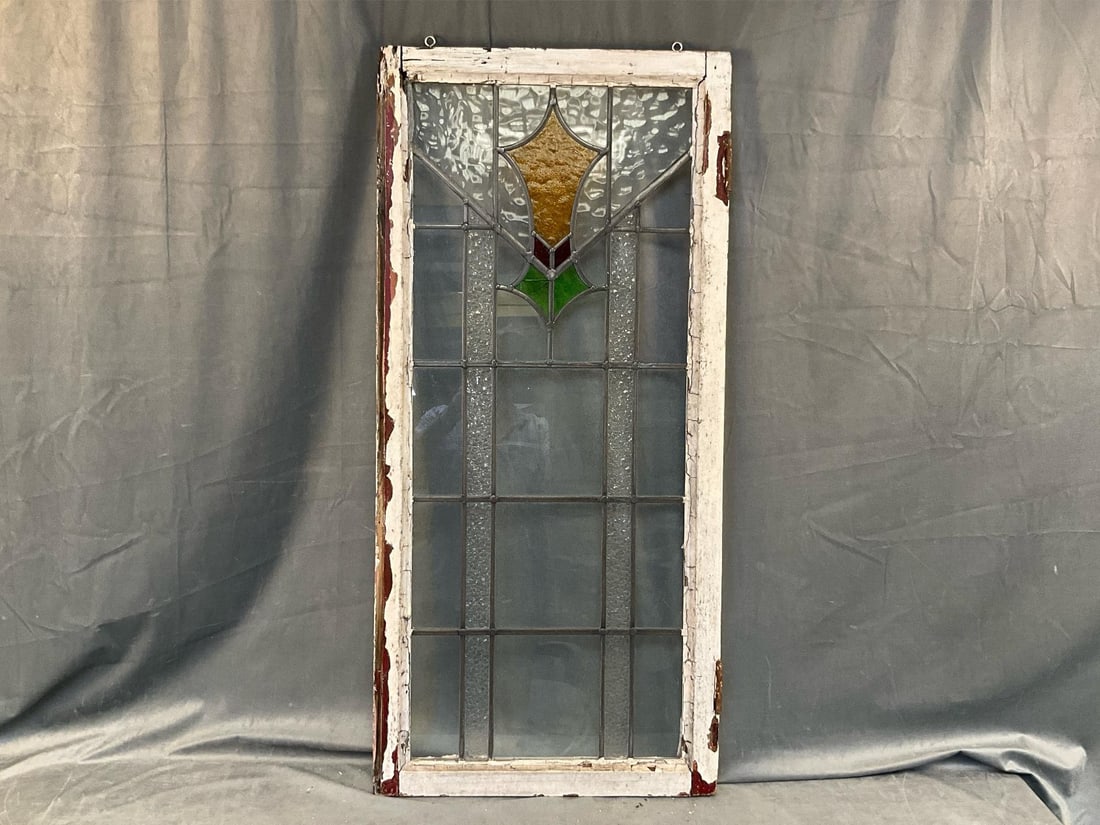 Antique Stained Glass Window: Early 20th century stained glass window. Window frame with peeling paint, two glass sections broken out and several cracks to center green glass section. Measures 20.5 inches wide x 2 x 44 inches