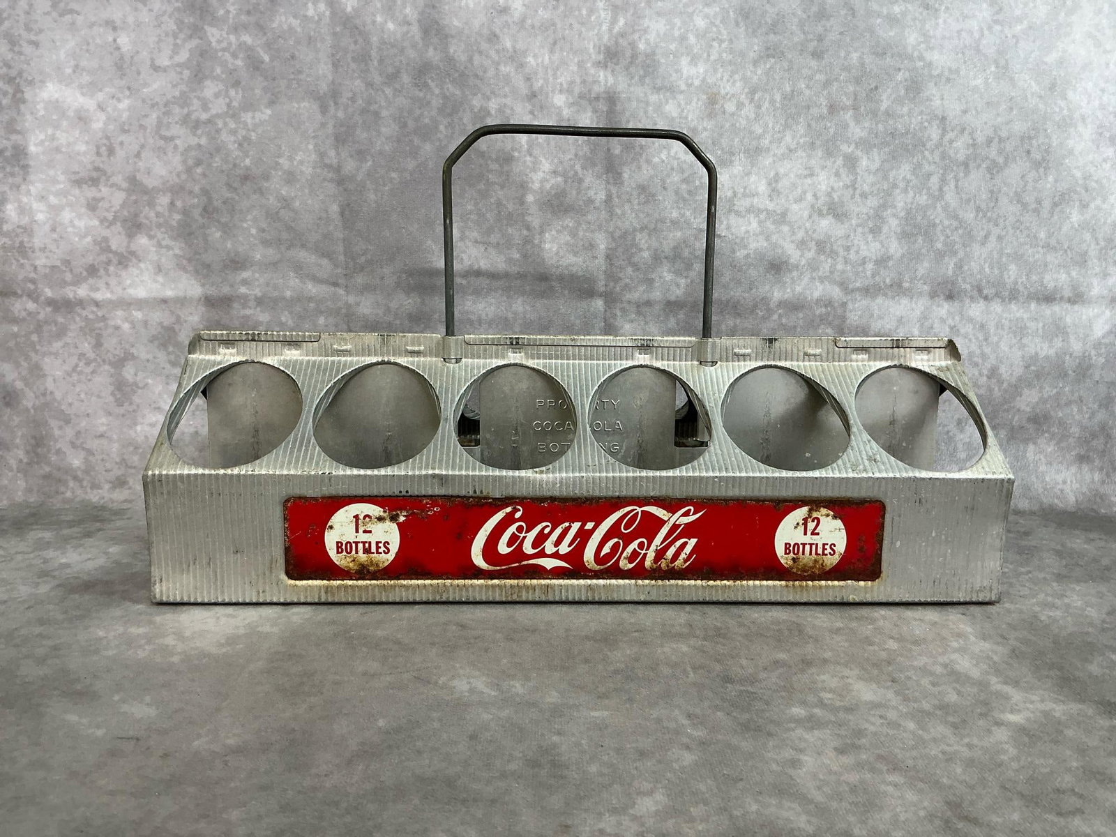 Coca-Cola Aluminum Carrier: 1950's twelve bottle carrier with handle. Aluminum with red and white logo panel. Some rust present otherwise in good condition. Measures 16.5 inches long x 5.25 x 5 inches tall, plus 5 inch handle.