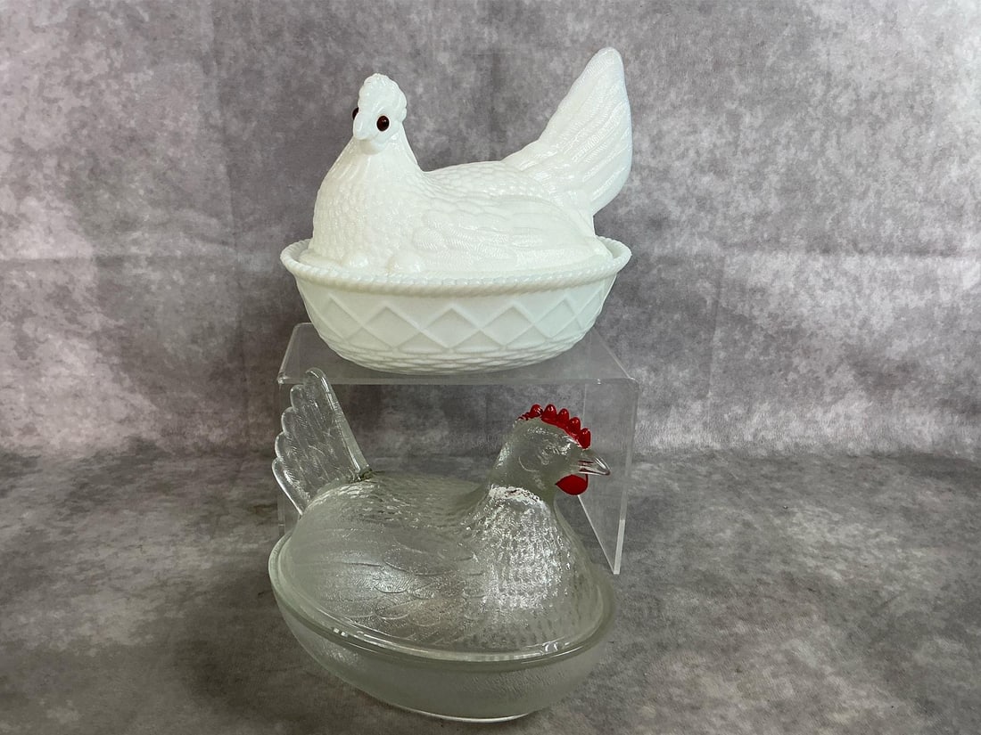 Hens on Nest: Two mid 1900's hens on nests. Westmoreland milk glass hen with brown glass eyes. Clear glass hen by Indiana glass with red comb. Clear hen has tiny chip on top edge and thumb size mark near tail