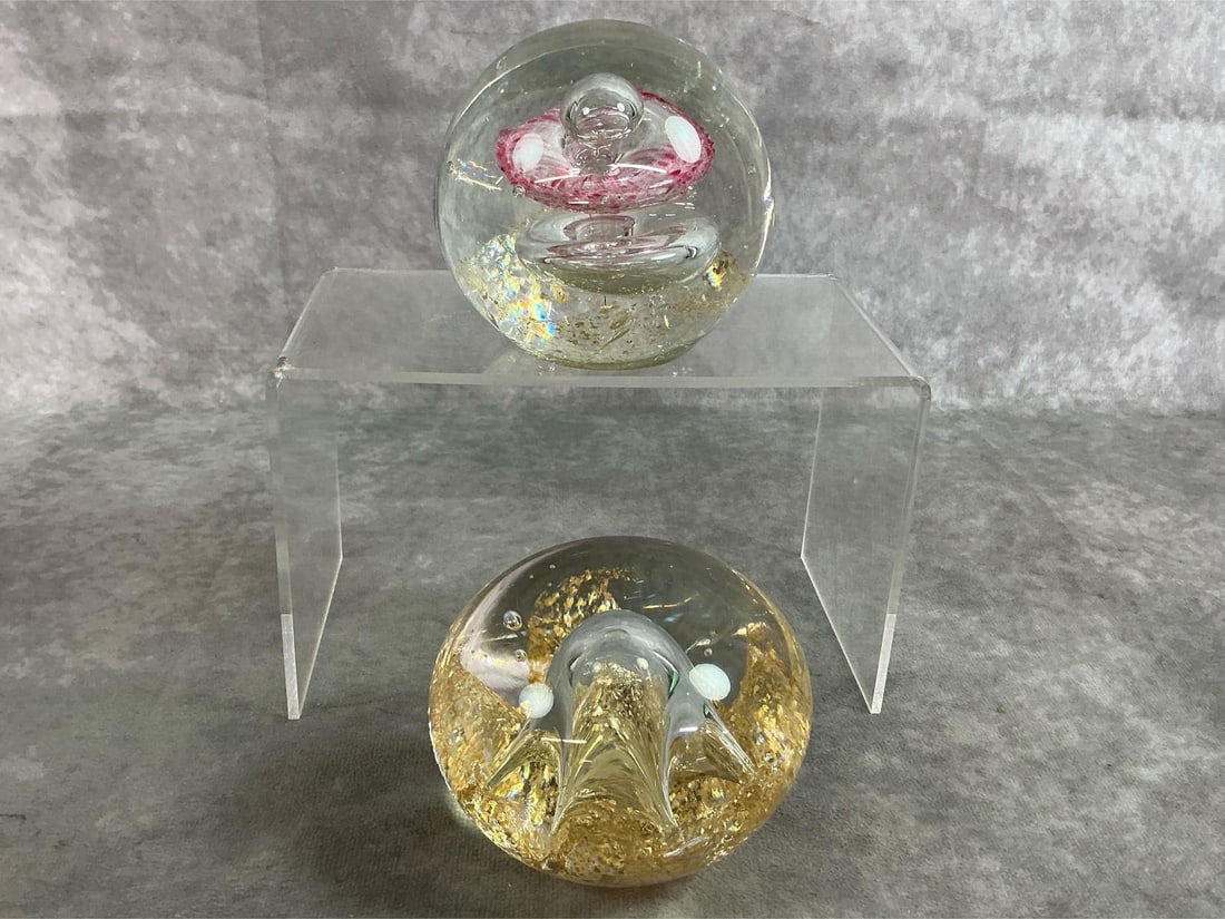 Murano Glass Paperweights: Two vintage paperweights made by Murano, star burst with gold flakes in clear glass and pink flower suspended over bubble with gold flecks. In good condition. Measure 4 inches wide x 4.5 inches tall.