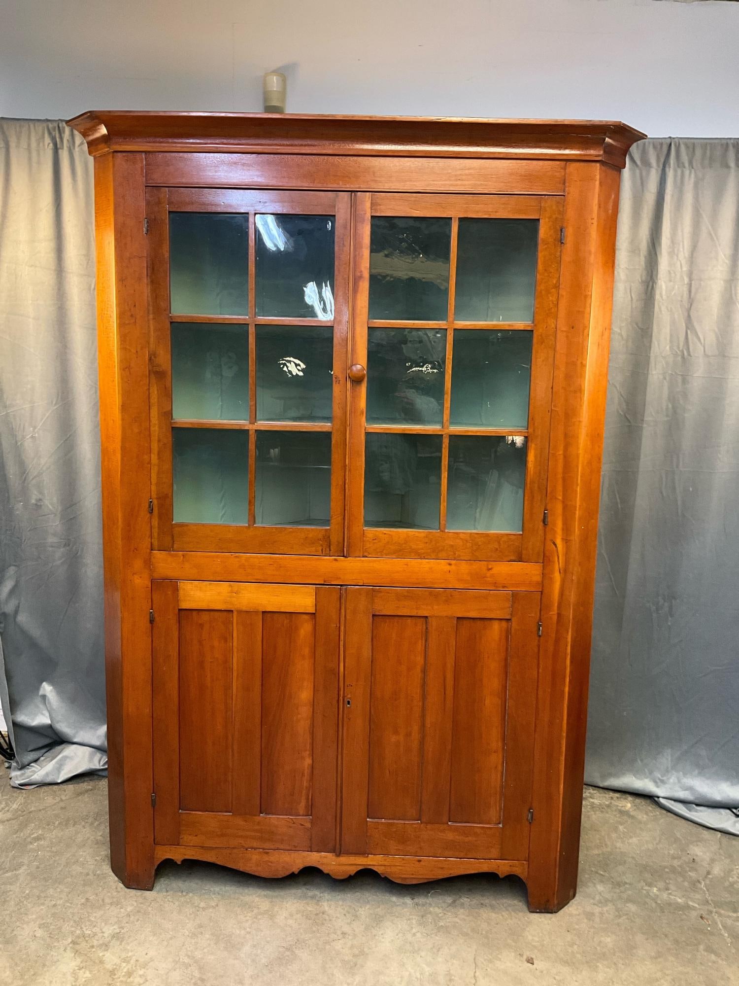 Antique Corner Cupboard: Early to mid-19th century one piece glazed 12 light corner cupboard. Cherry with white pine secondary wood and later polyurethane finish over original. Two paneled lower doors over scrolled base. Penn