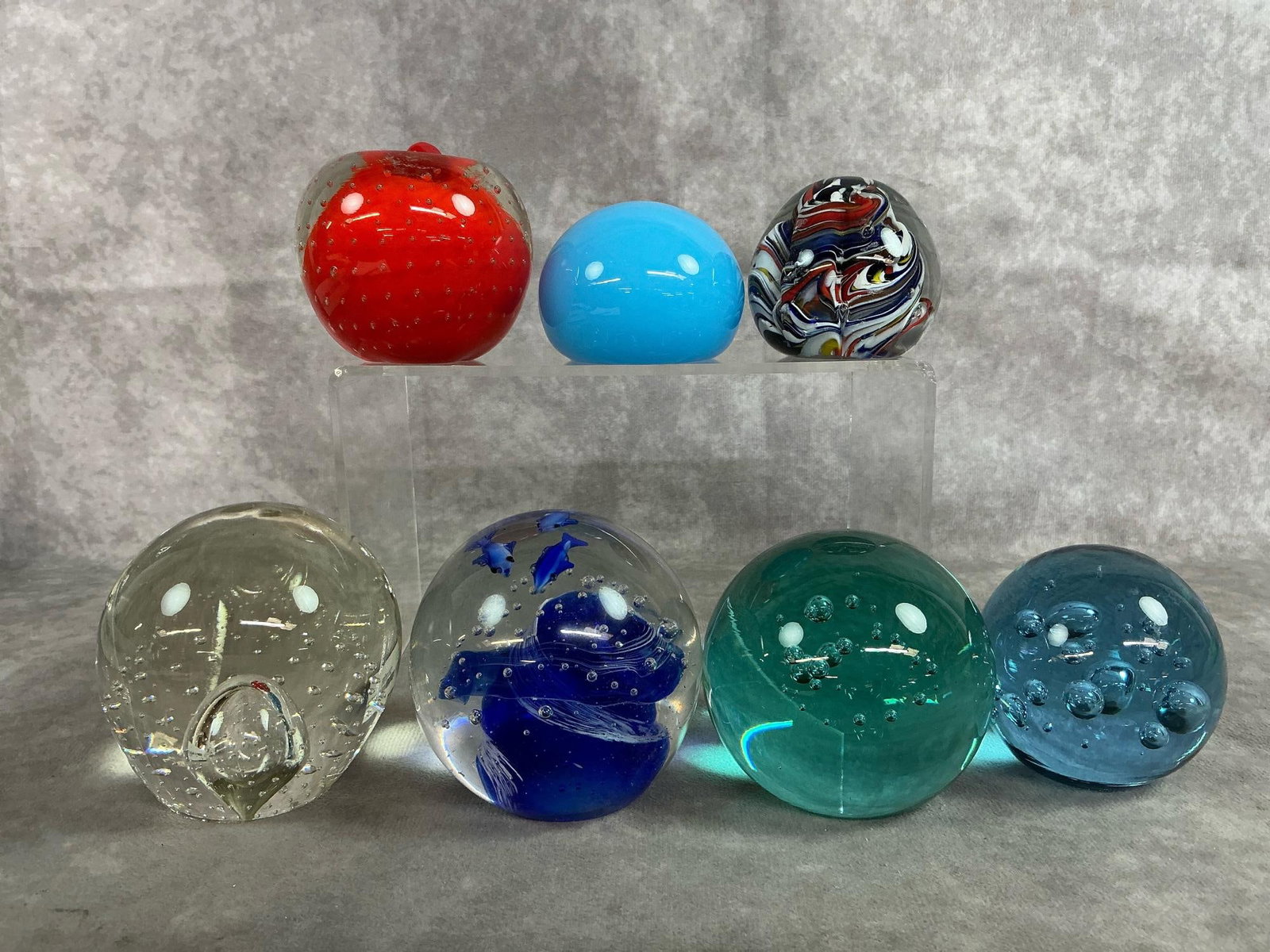 Art Glass Collection: Seven vintage paperweights. Variety includes red apple Bullicante controlled bubble art, and clear glass marked Eickholt 2004. Dark blue swirl with fish, multi-colored swirl orb, and more. In good