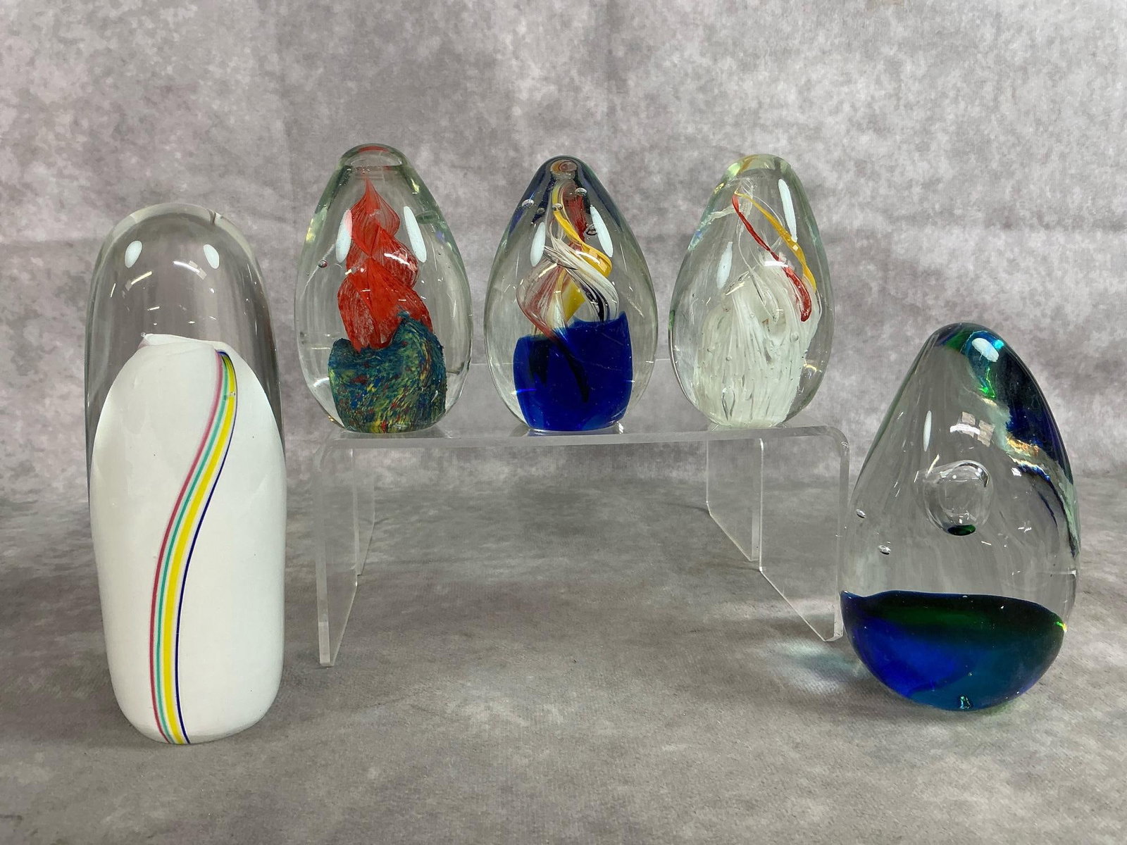 Murano Style Art Glass: Five vintage art glass paperweights. Includes white with multi-colored stripe bullet shaped paperweight, and four sided blue and green controlled bubble art glass. Three egg shaped small Murano-style 