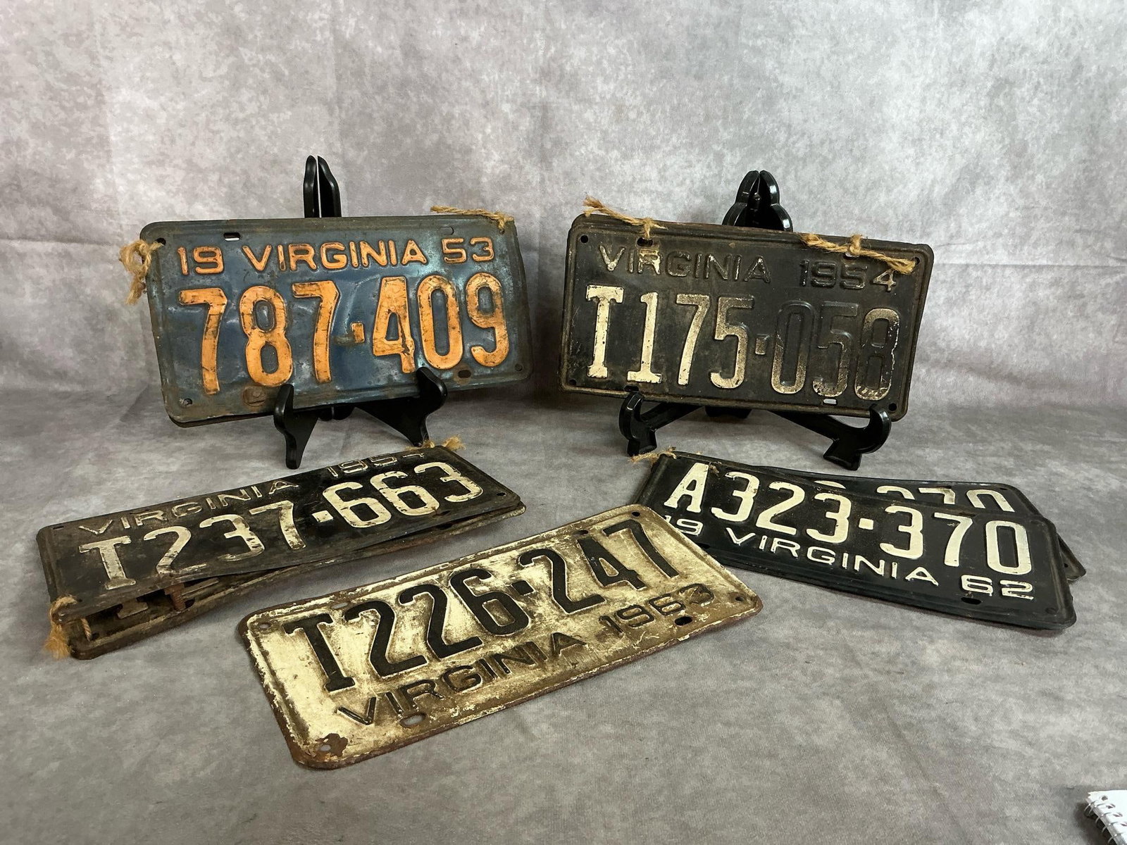 Vintage License Plates: Nine Virginia used license plates. Three sets include 1953, 1954 x 2, 1962, and a single 1963 plate. Rust and discoloration present. Plates measure 11.5 inches long x 6 inches tall.