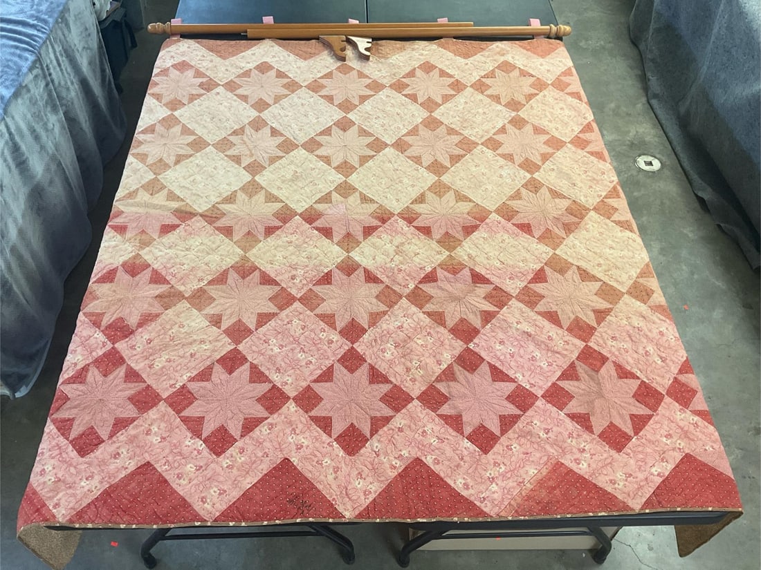 Star Pattern Quilt: Vintage homemade star pattern quilt, machine stitched and quilted. Front is made from early 1900s feedsack material, with pink ribbon loops, and a wooden rod with brackets for hanging. Has some