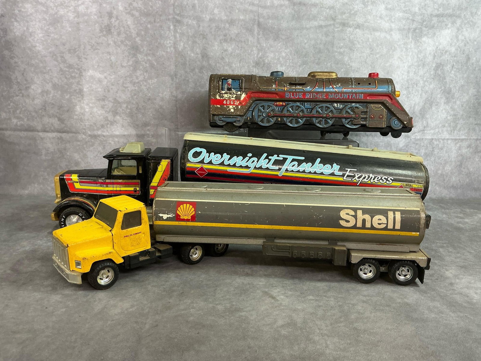 Collectible Tankers & Tin Locomotive: Three mid to late 1900's toy trucks and train. Blue Ridge Mountain tin lithography battery operated locomotive (untested). Nylint Overnight Tanker Express metal truck and tanker, 1:18 scale. Also,