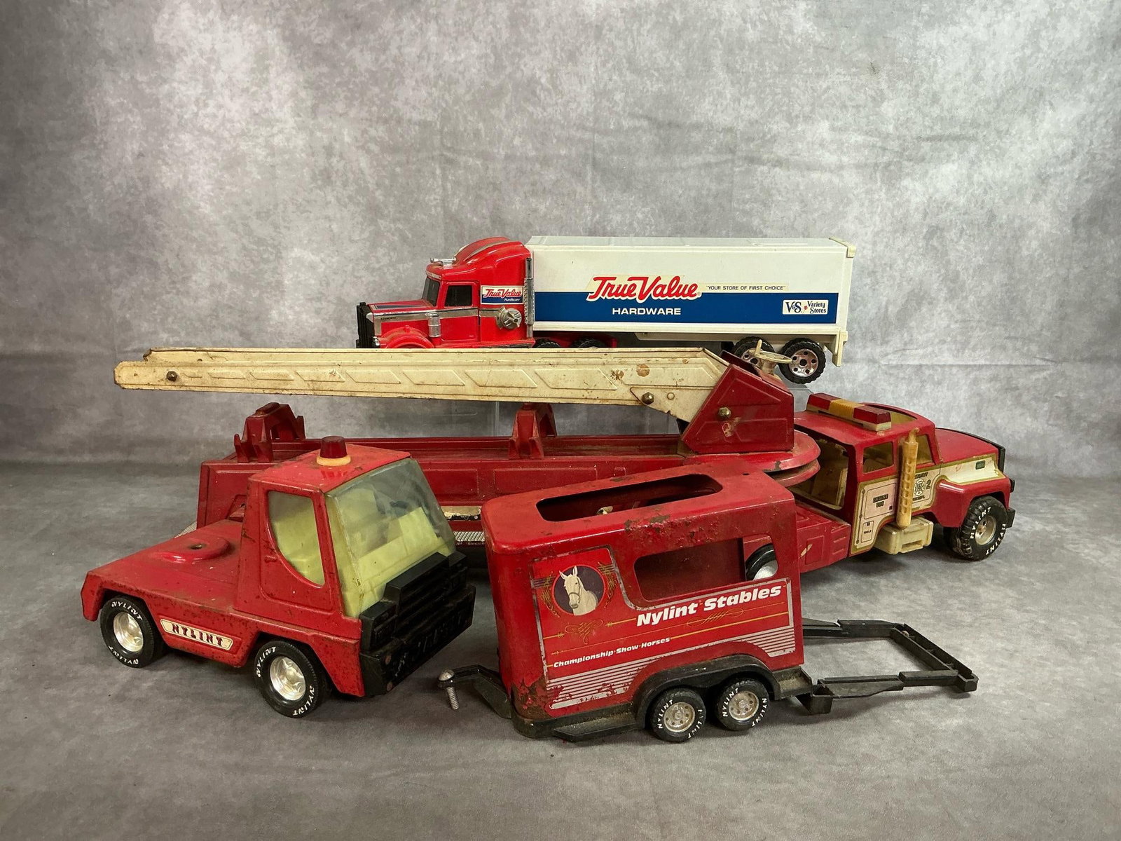 Nylint & Buddy L Toy Trucks: Three trucks and horse hauler from late 1900's. Includes Buddy L Kenworth "True Value" cab and trailer, Nylint Fire Department #2 pressed steel ladder truck, and Nylint Fire truck cab. Also, Nylint St