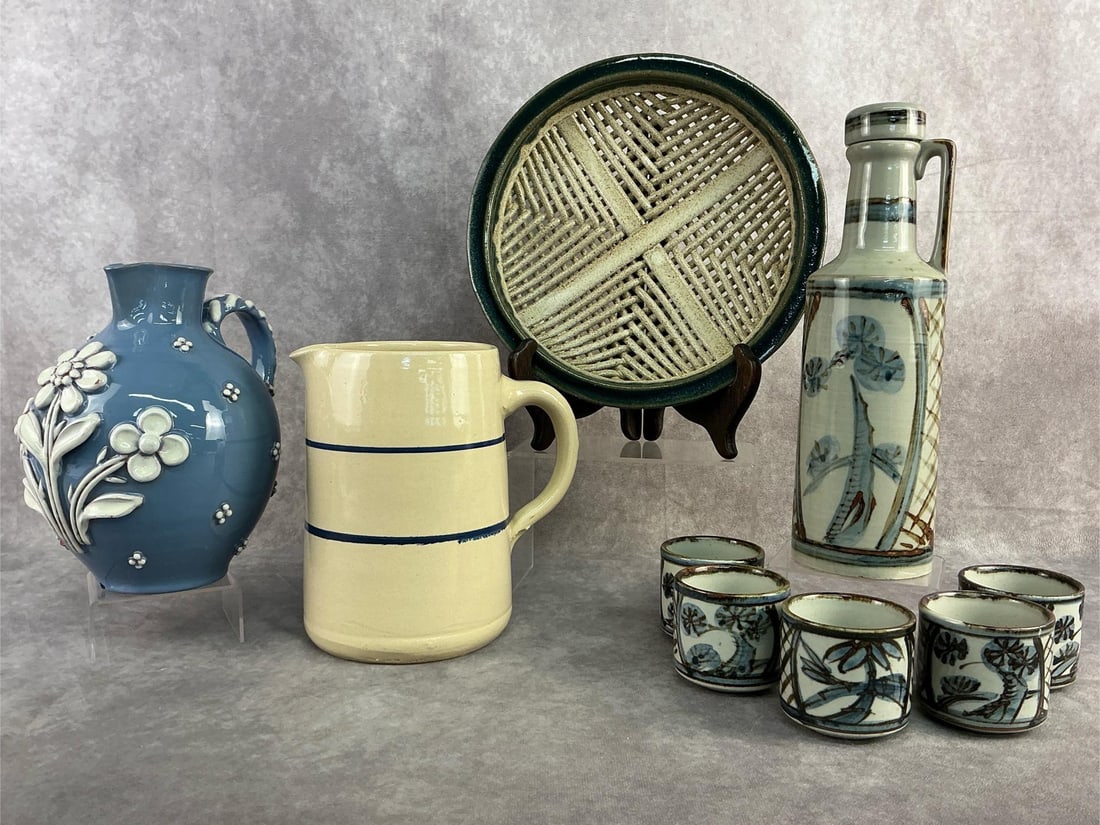 Art Pottery Pitchers, Decanters & More: Nine art pottery items. The blue floral pitcher has two small chips, otherwise all in good condition. The woven pottery dish measures 10.25 inches in diameter.