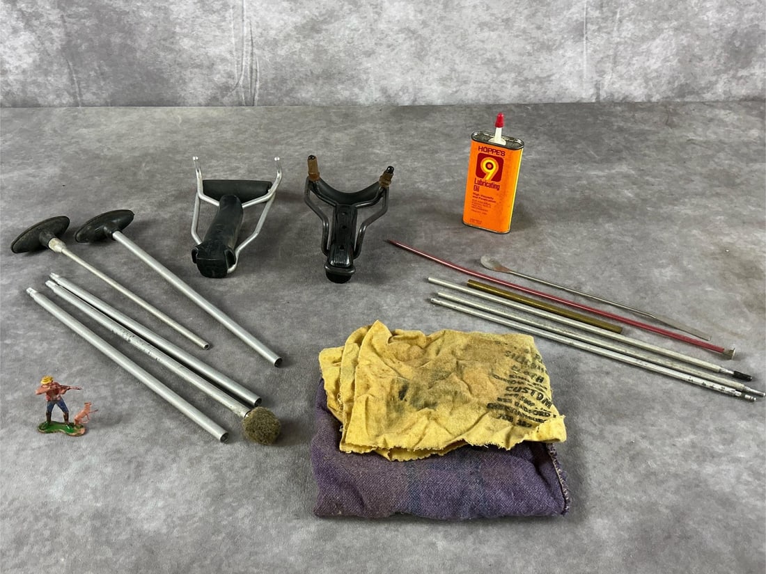 Hoppe's Gun Cleaning Accessories And Slingshots: Gun cleaning supplies by Hoppes, slingshot frames, and miniature figure in mixed colors. In fair condition with missing elastic bands, heavy cloth soiling. Slingshot measures 6 1/2 inches long X 4