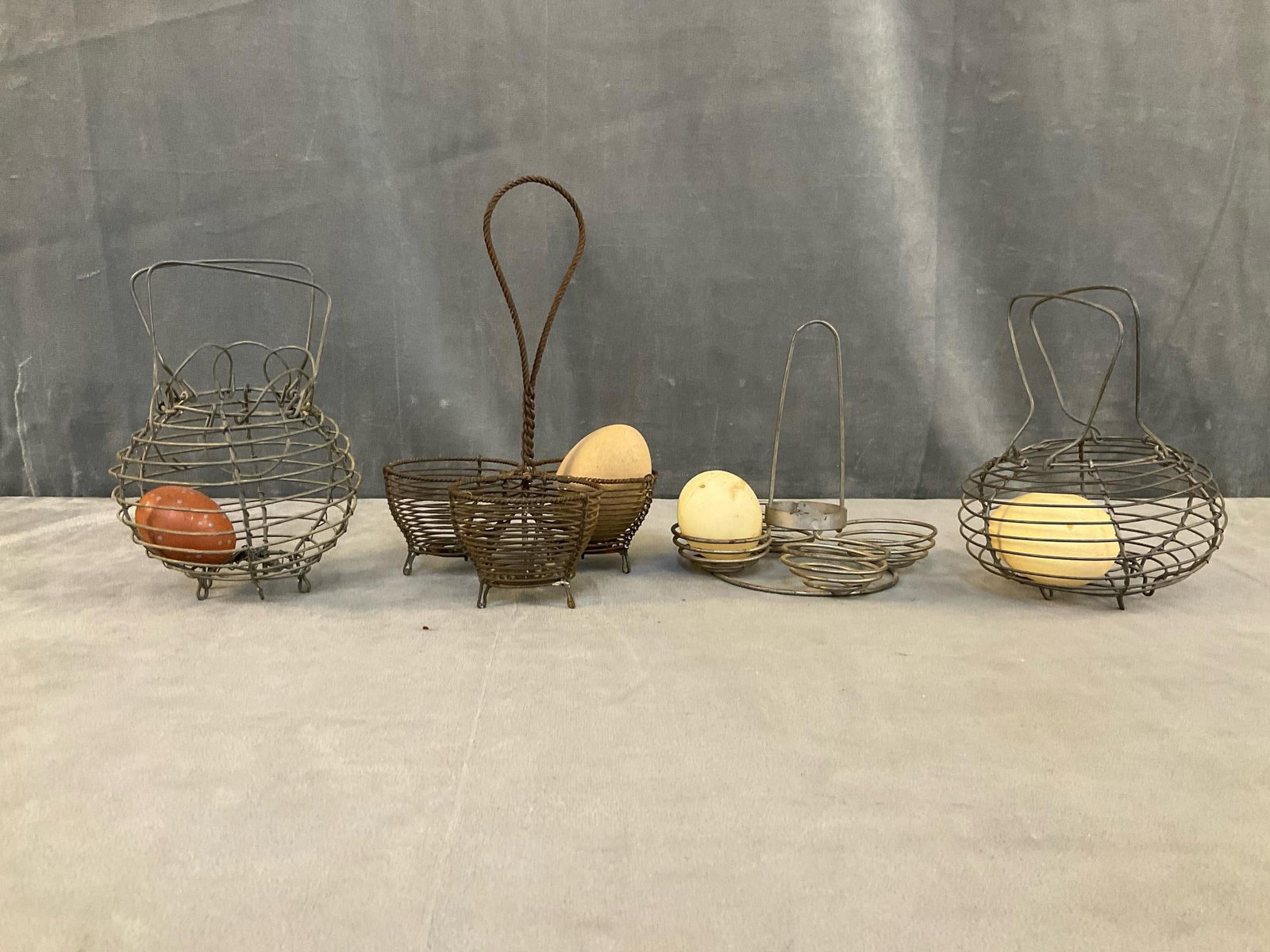 Wire Egg Baskets: Four early 20th century miniature wire egg carriers/baskets with two wooden and two plastic eggs. One basket with several bent wires, otherwise good condition. Largest basket measures 4 inches in diam