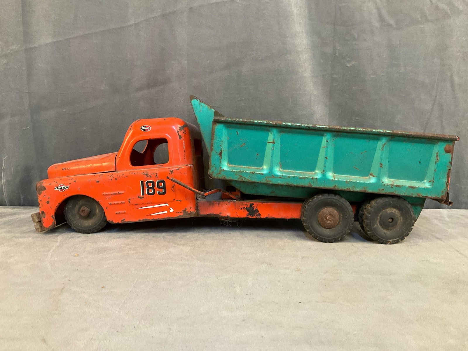 Structo Metal Dump Truck: 1950's pressed steel Structo green and red/orange dump truck. Rust, missing paint, bent chassis, missing front bumper and bed does not lift. Measures 21 inches wide x 8 x 7 inches tall.