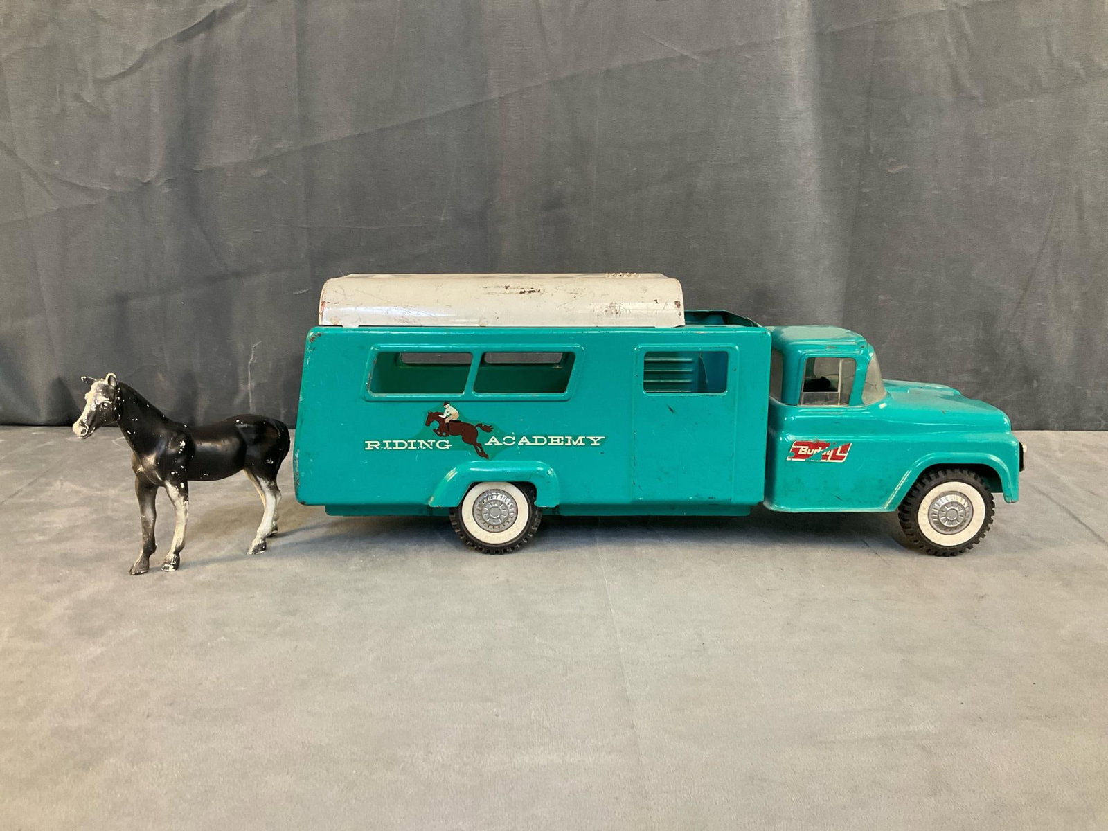 Buddy L Metal Truck: 1960's pressed steel Buddy L "Riding Academy " toy metal horse hauler truck. Teal and white painted with plastic horse. Truck missing rear ramp, skylight, cattle guard and has scratches. Measures