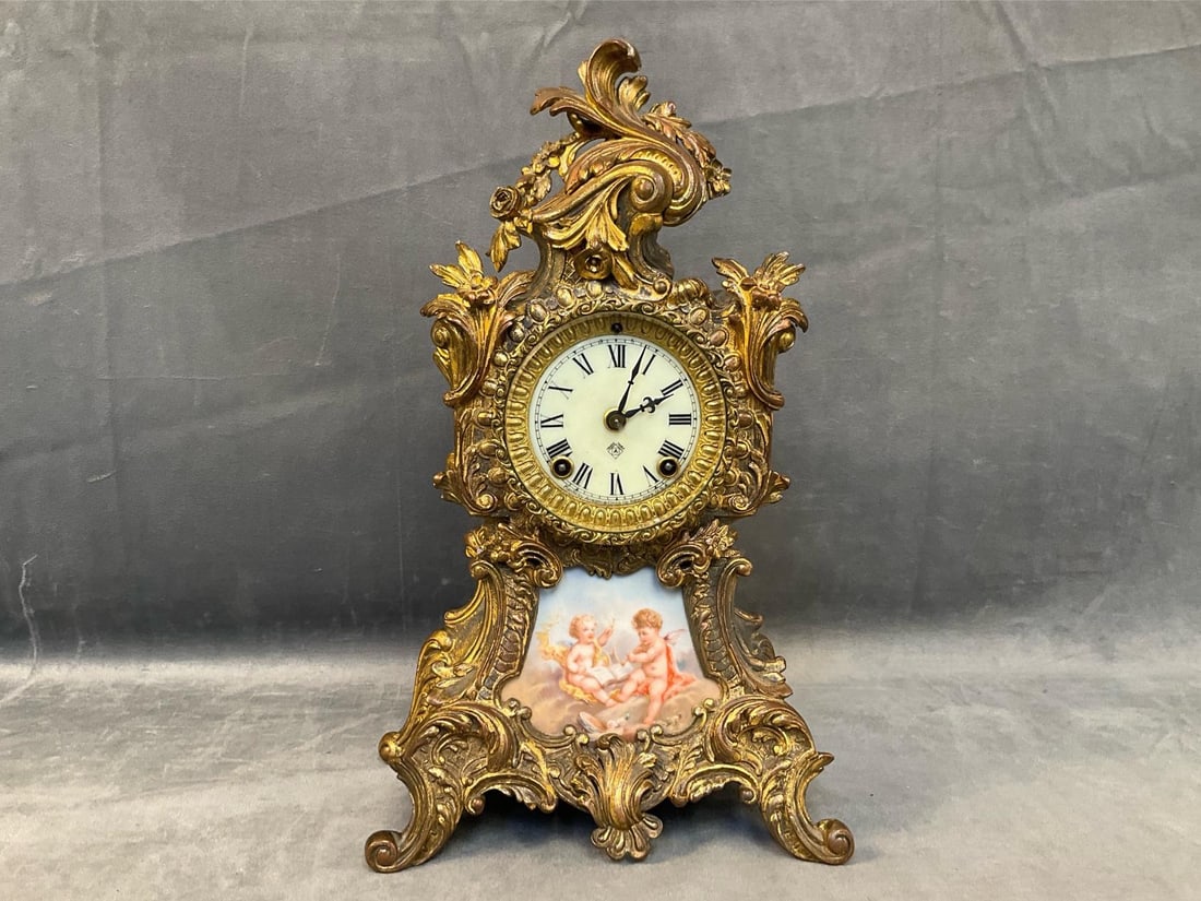 Mantel Clock: Early 20th century Ansonia ormolu gilt metal mantel clock in the French Rococo manner. Enameled face with Ansonia Trade Mark and painted porcelain insert depicting two putti. Good working condition.