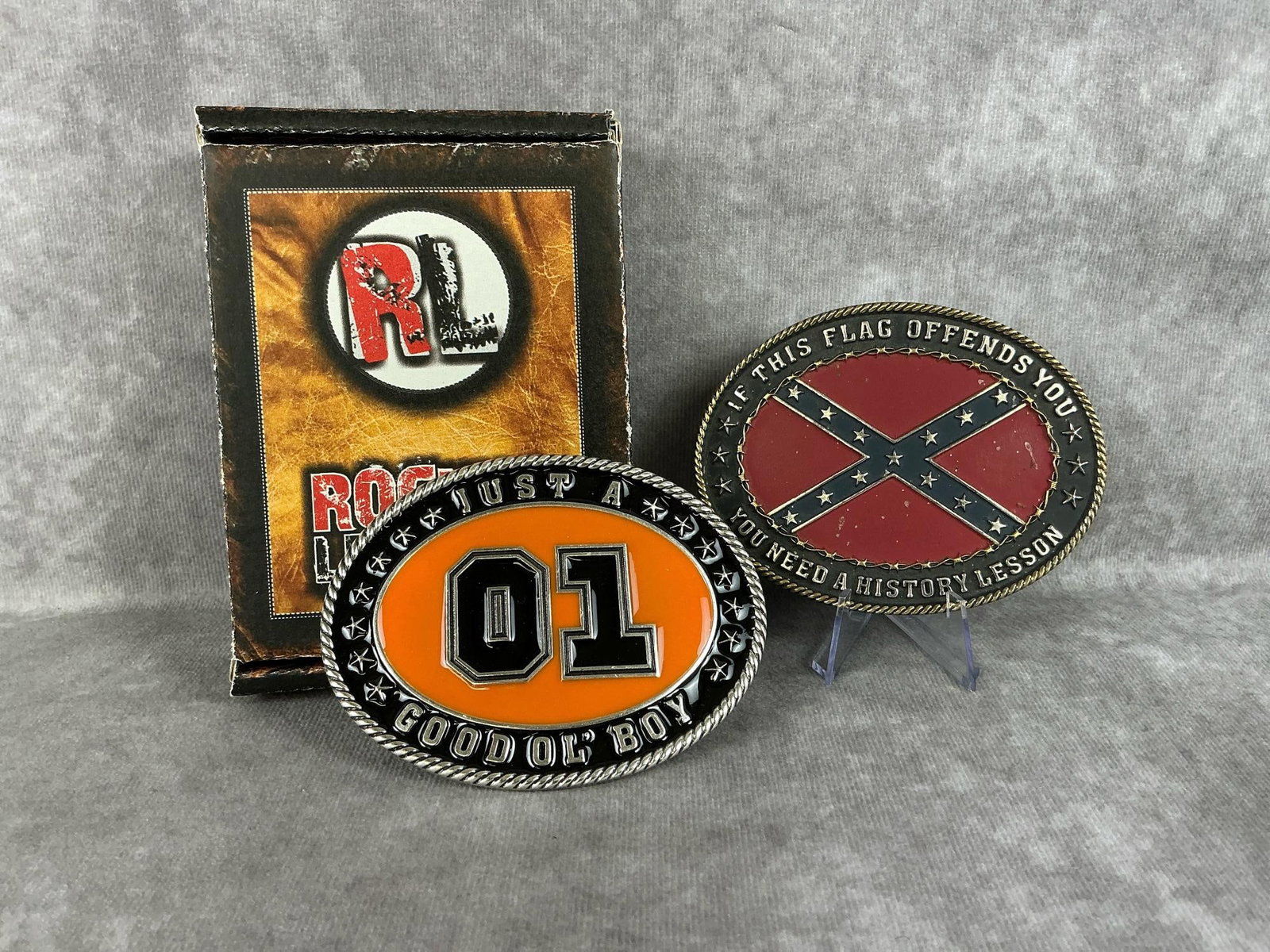 Belt Buckles: Two modern metal belt buckles made by Rockin Leather. Includes the rebel flag and a Dukes of Hazard Good O' Boy buckle, and one original box. Good condition, box measures 5.5 inches wide x 1.25 x 4