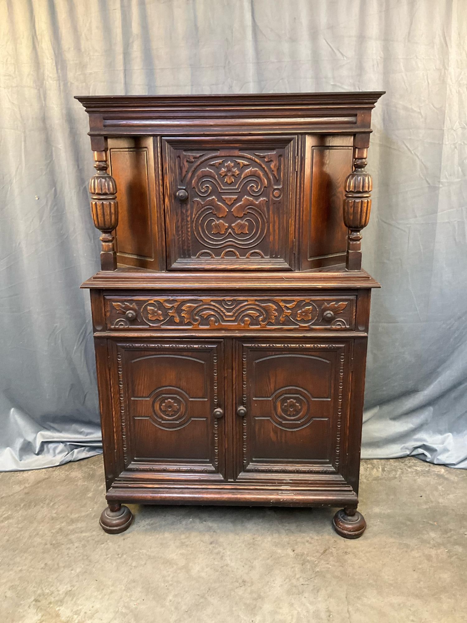 Court Hutch: Early 20th century Jacobean/Tudor Revival style carved oak court cupboard hutch with one drawer between one door over two lower doors. Lower storage area with one shelf not in place, missing upper