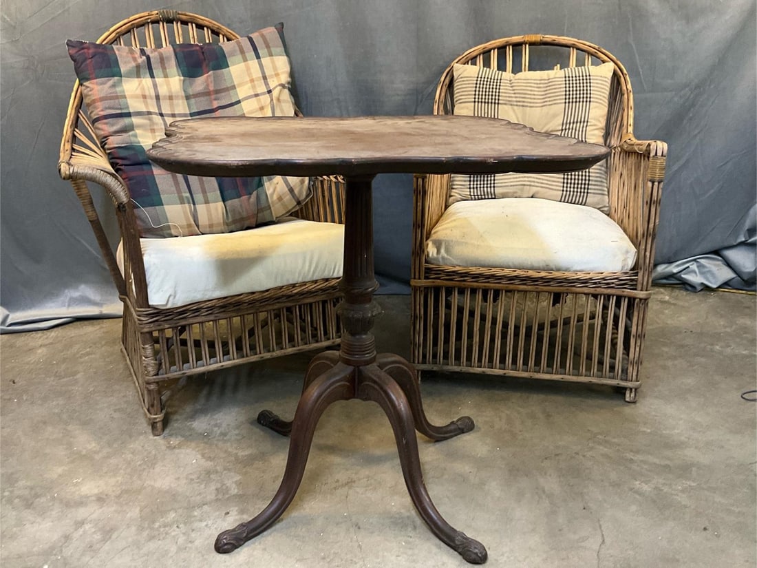 Porch Furniture: Three mid-20th century pieces of porch or sunroom furniture. Two wicker rattan lounge armchairs. Both missing some areas with soiled upholstery. Mahogany reproduction Chippendale Georgian carved tea
