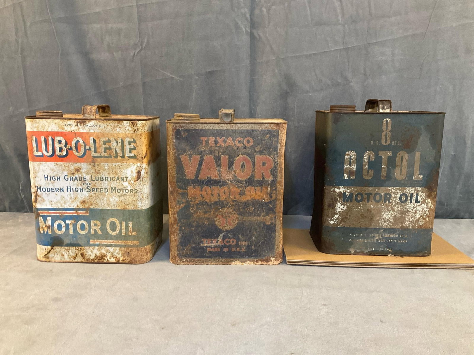 Oil Cans: Three mid-20th century two gallon metal oil cans. "LUB-O-LENE" motor oil, "Texaco / Valor" motor oil, and "Acto" motor oil. Rusted, weathered, dented, used condition. "LUB-O-LENE" with hole to bottom