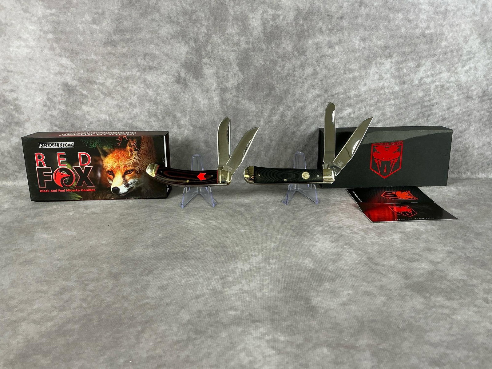 Rough Rider & Cobratec Knives: Modern Rough Rider Red Fox knife with black and red micarta handles, and a Cobratec VG10 trapper. Both in original boxes, good condition. Largest box measures 6.25 inches wide x 1.75 x 3 inches tall.