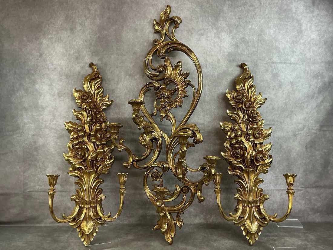Ornate Wall Sconces: Three late 1900's gold gilt wall sconces. Molded resin by Syroco with flowers and curlicues. Largest has five candle holders and each side sconce has 2 candleholders. Some gold paint missing on one