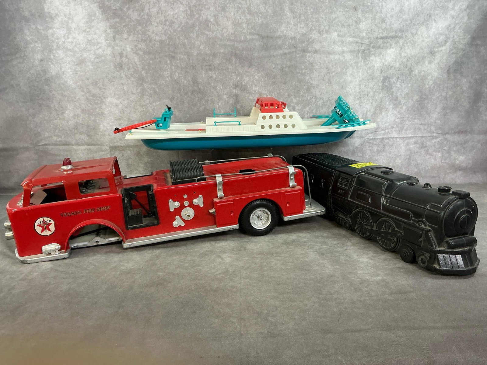 Vintage Toy Truck, Boat, & Train: Three mid 1900's toys. Texaco Fire Chief metal fire engine (missing front wheels and ladder extension). Includes black plastic "whistling" Marx RR 333 locomotive, and plastic Ferry Boat. Boat has