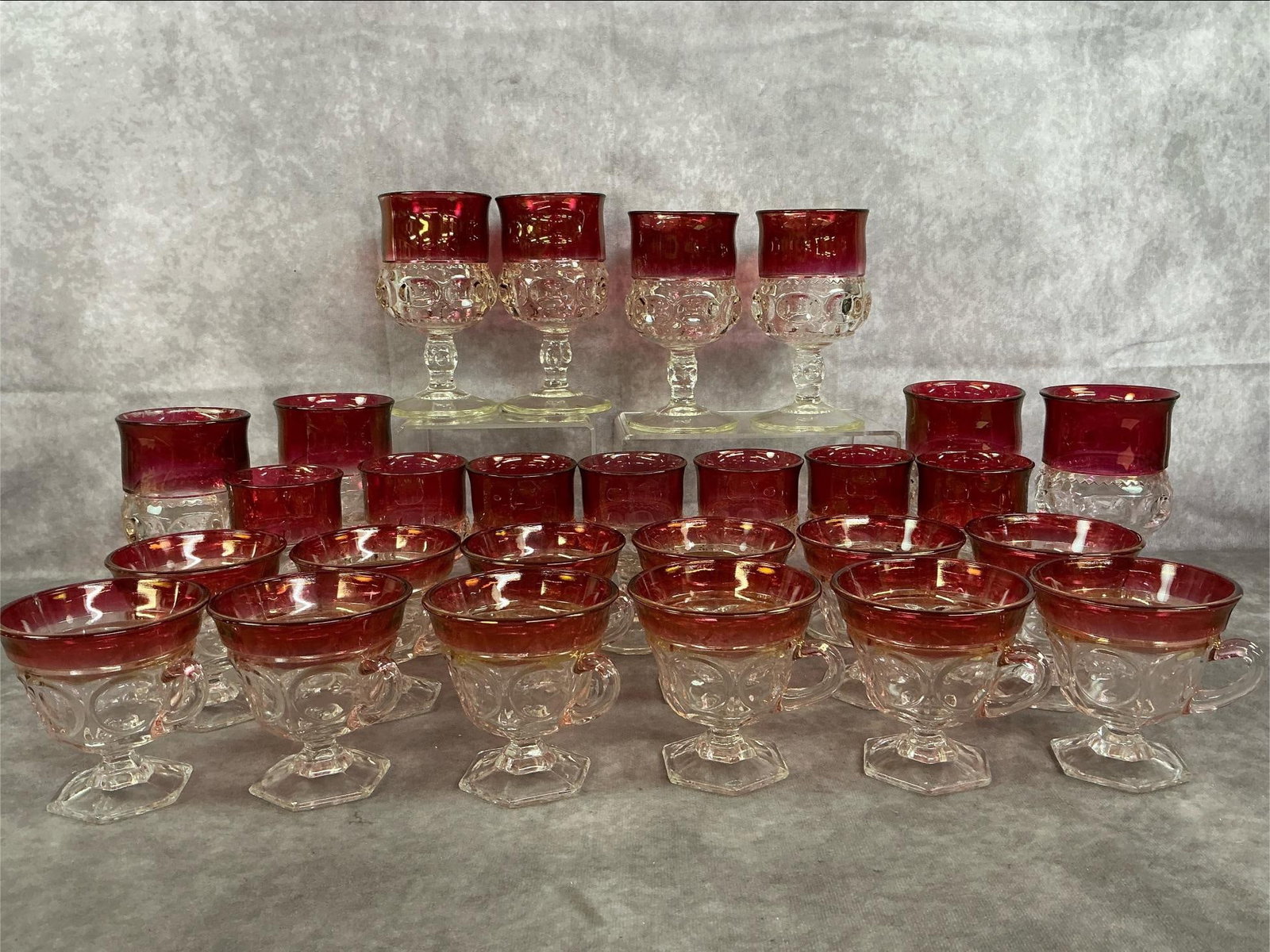 Indiana Glassware: Twenty-seven mid century Indiana Glass glasses. King's Crown Ruby thumbprint glasses, including 8 water goblets, 7 small goblets, and twelve punch cups. Slight color loss around rims, otherwise in