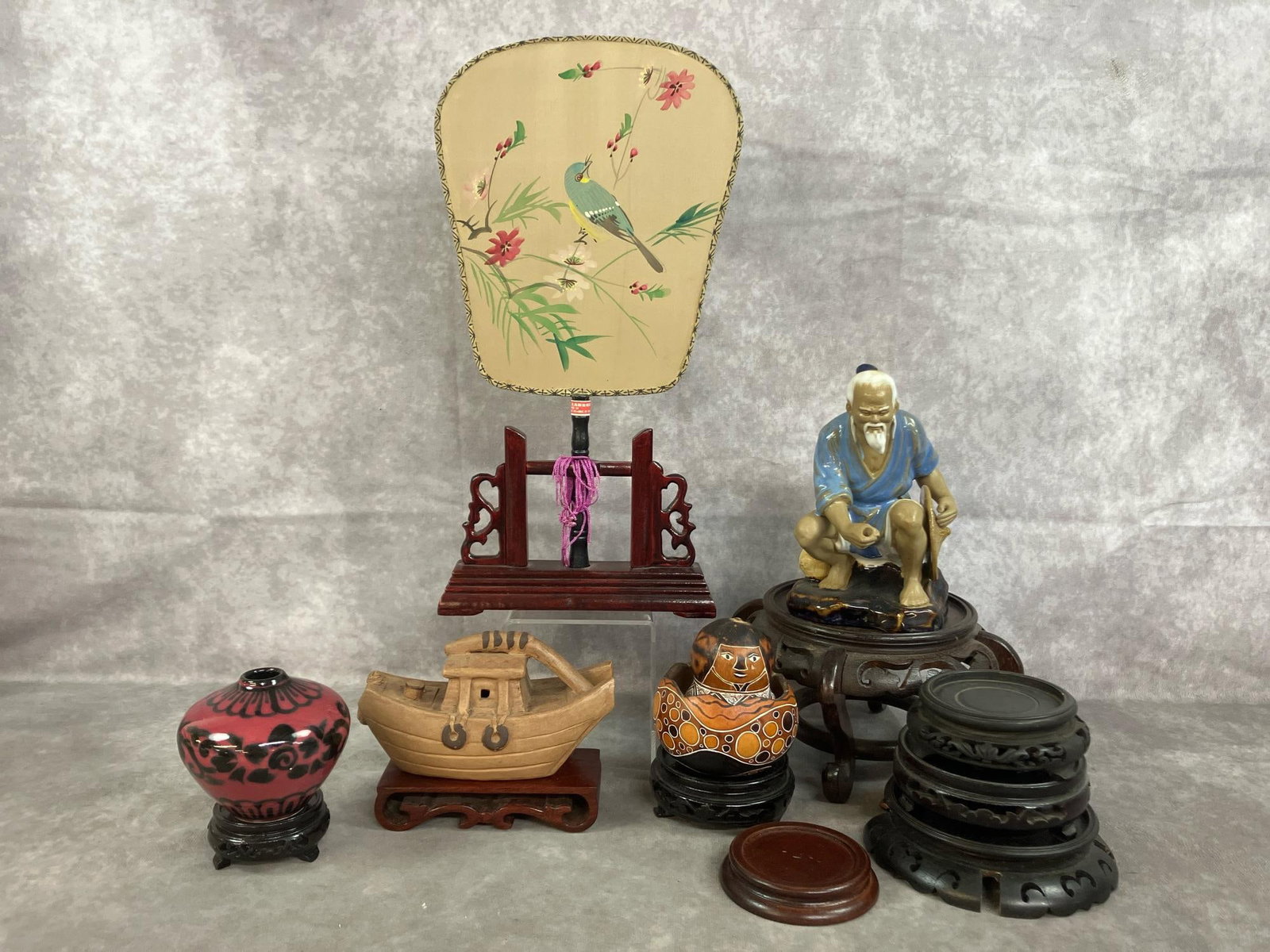 Chinese Fan, Mudman, Boat & More: Ten mid to late 1900's Chinese collectibles. Silk paddle fan in carved wooden stand, Shiwan Mudman ceramic figure, Peruvian hand carved gourd figure, and clay boat on stand. Includes black and rose co