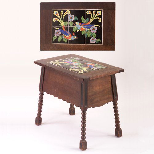 TAYLOR Tile-top sewing table with a six-tile panel: TAYLOR Tile-top sewing table with a six-tile panel depicting birds of paradise in bright polychrome on black ground, mounted in a flip-top Mission table with turned legs. A few short scratches to tile