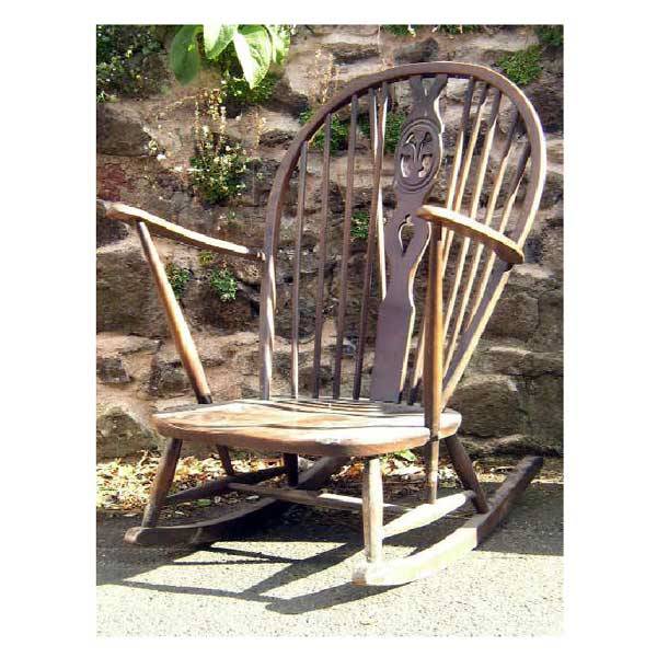 Furniture - An Ercol large beech windsor rocking: Furniture - An Ercol large beech windsor rocking chair with hoop back supported on spindles, flanking a fleur-de-lis pierced splat, with shaped arms and solid seat, raised on turned legs with shaped r