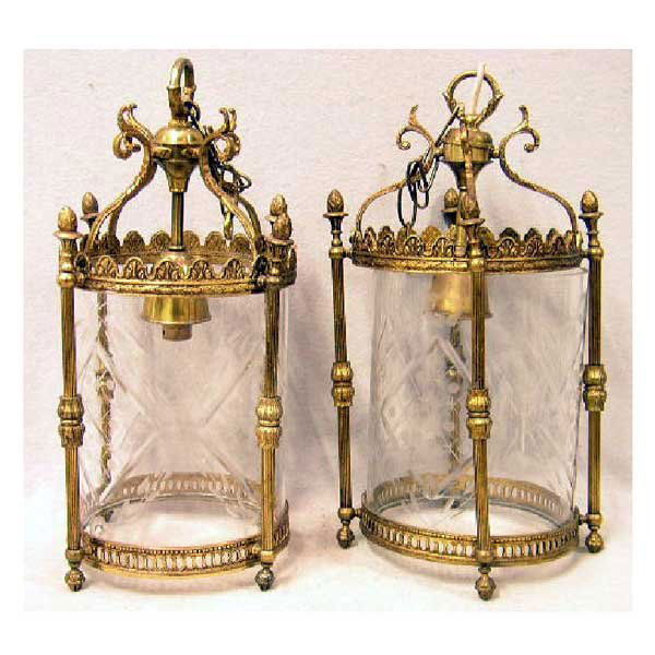 Lighting - A pair of Edwardian brass hall lantern: Lighting - A pair of Edwardian brass hall lanterns, with tubular cut glass enclosures framed by four reeded pillars, having pierced rim and leaf moulded crest supporting a tubular lamp column on scrol