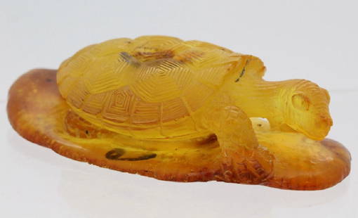 Natural Baltic Honey Amber Carved Turtle Figurine 21.1g: Carved natural amber figurine. Features a carving of a turtle or tortoise on a platform. Crafted from one solid piece of natural Baltic amber with a semi translucent honey hue. Measures 3.25" x 1.75".